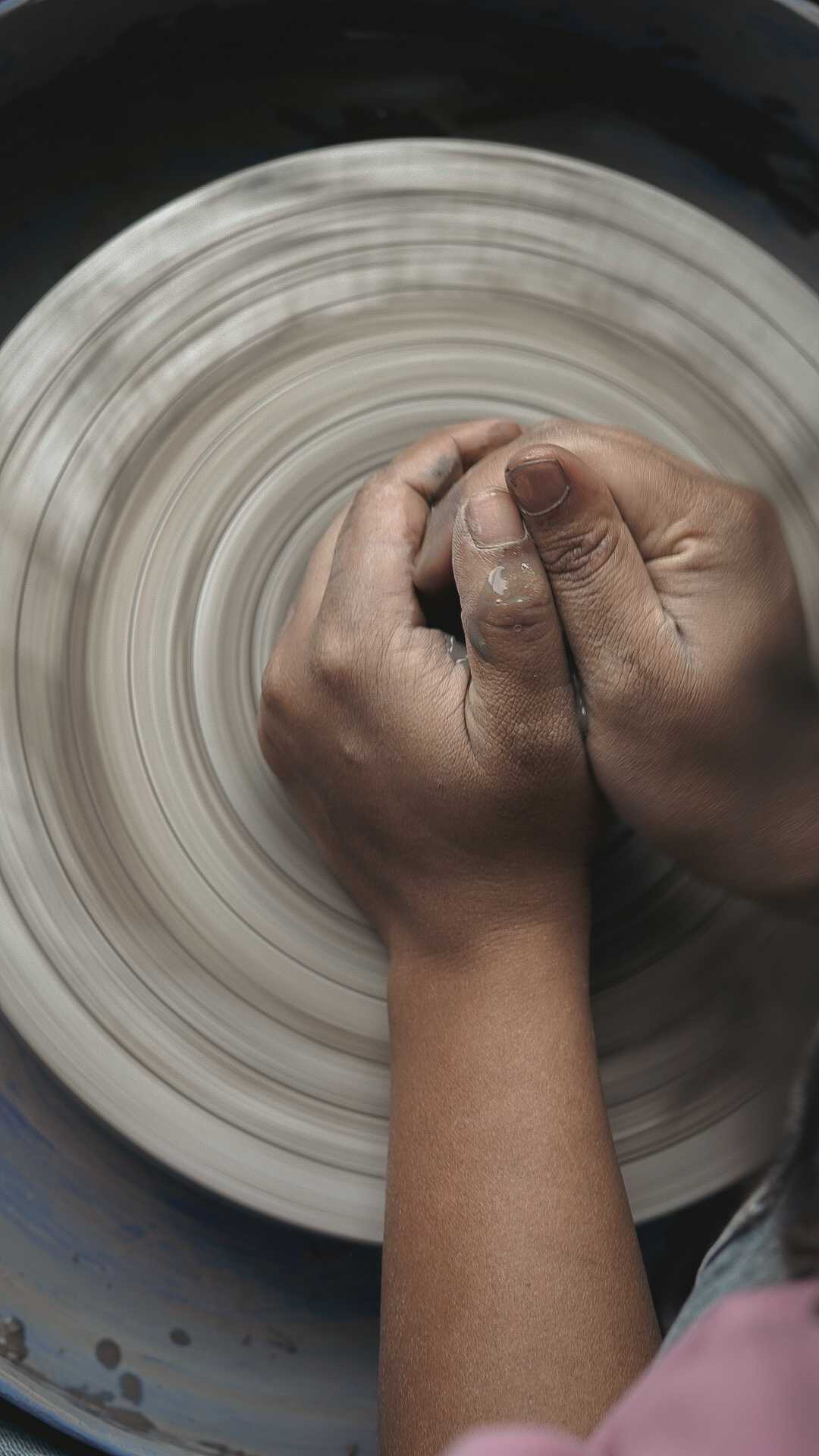 Hands centering wet clay on a spinning wheel with motion blur