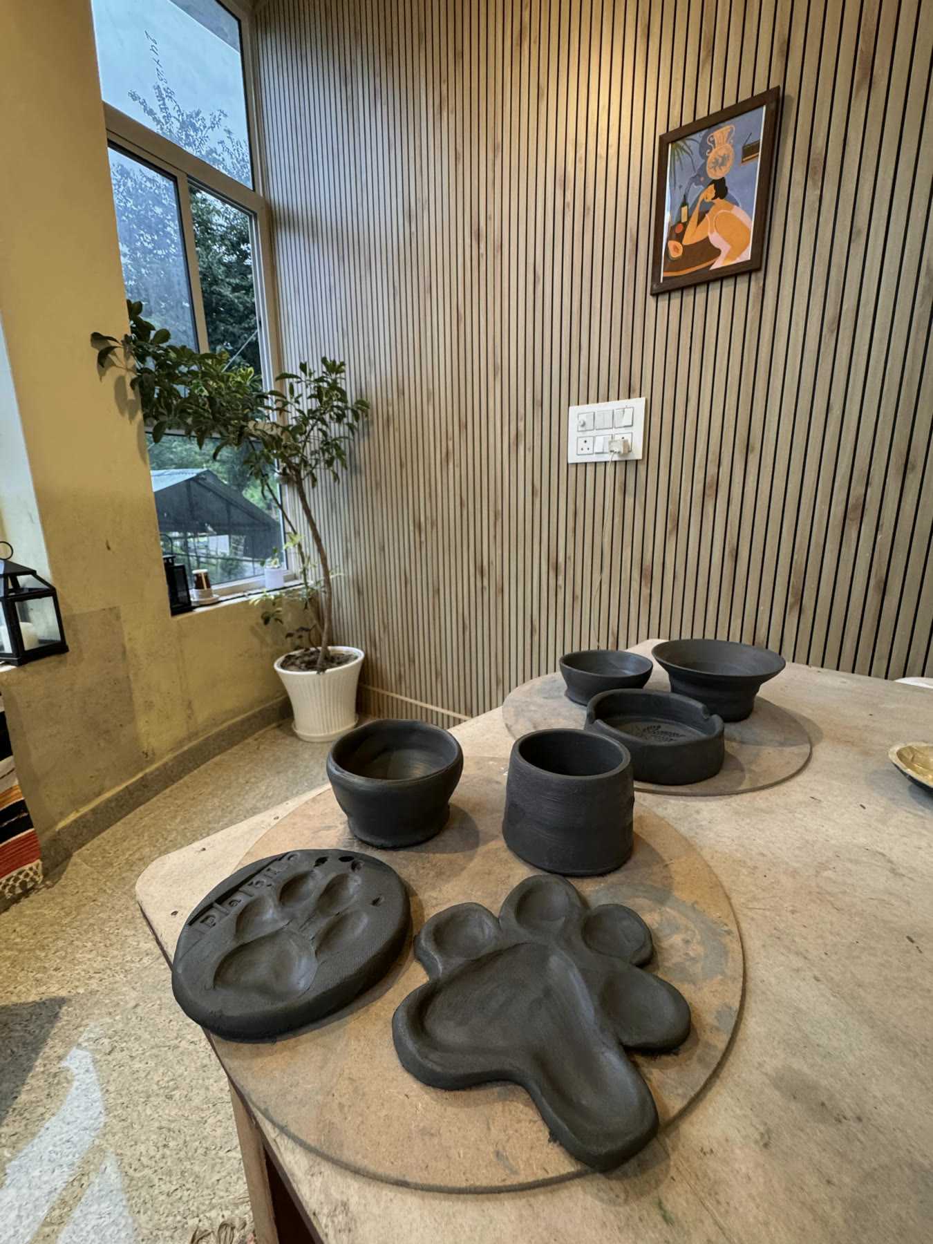 Dark clay dishes pressed with paw prints, drying on the work surface