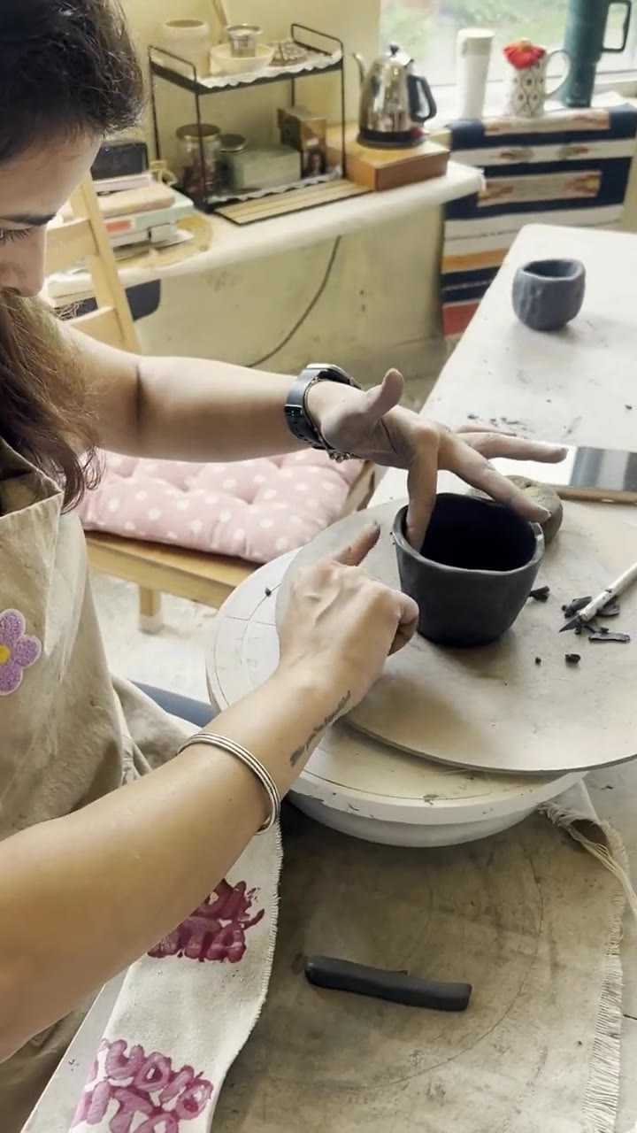 Overhead view of hands trimming the foot of a small dark bowl with a wooden tool