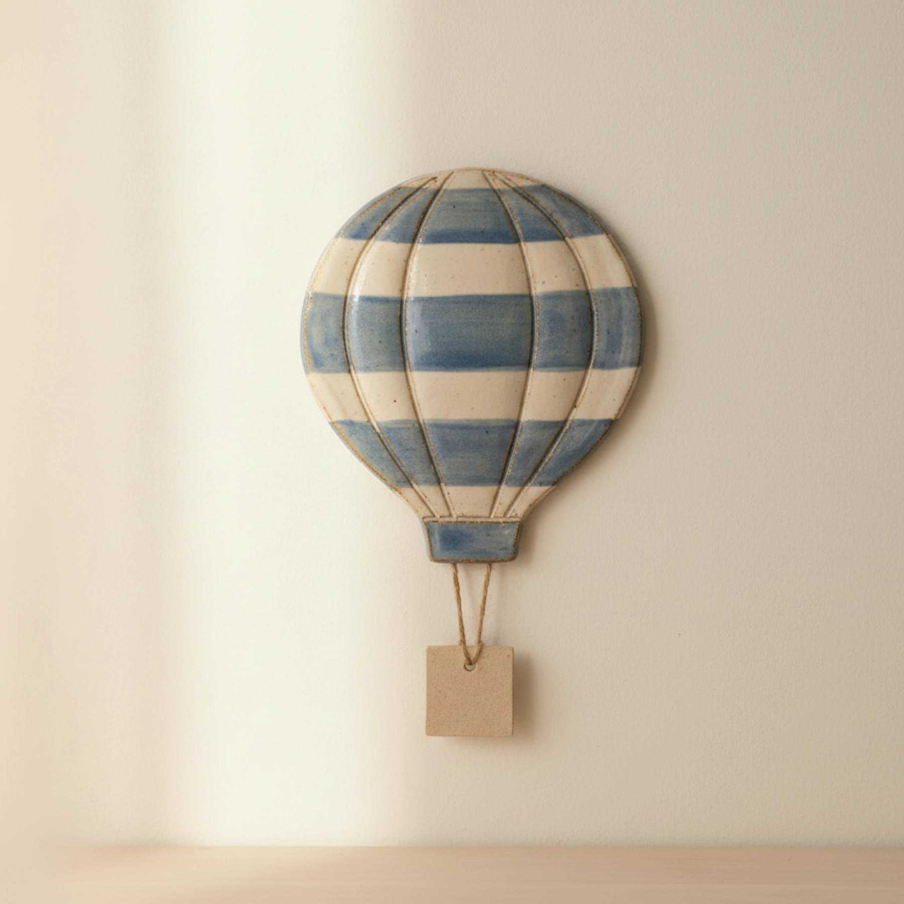 Illustration of a striped ceramic hot-air balloon wall hanging with a small tag
