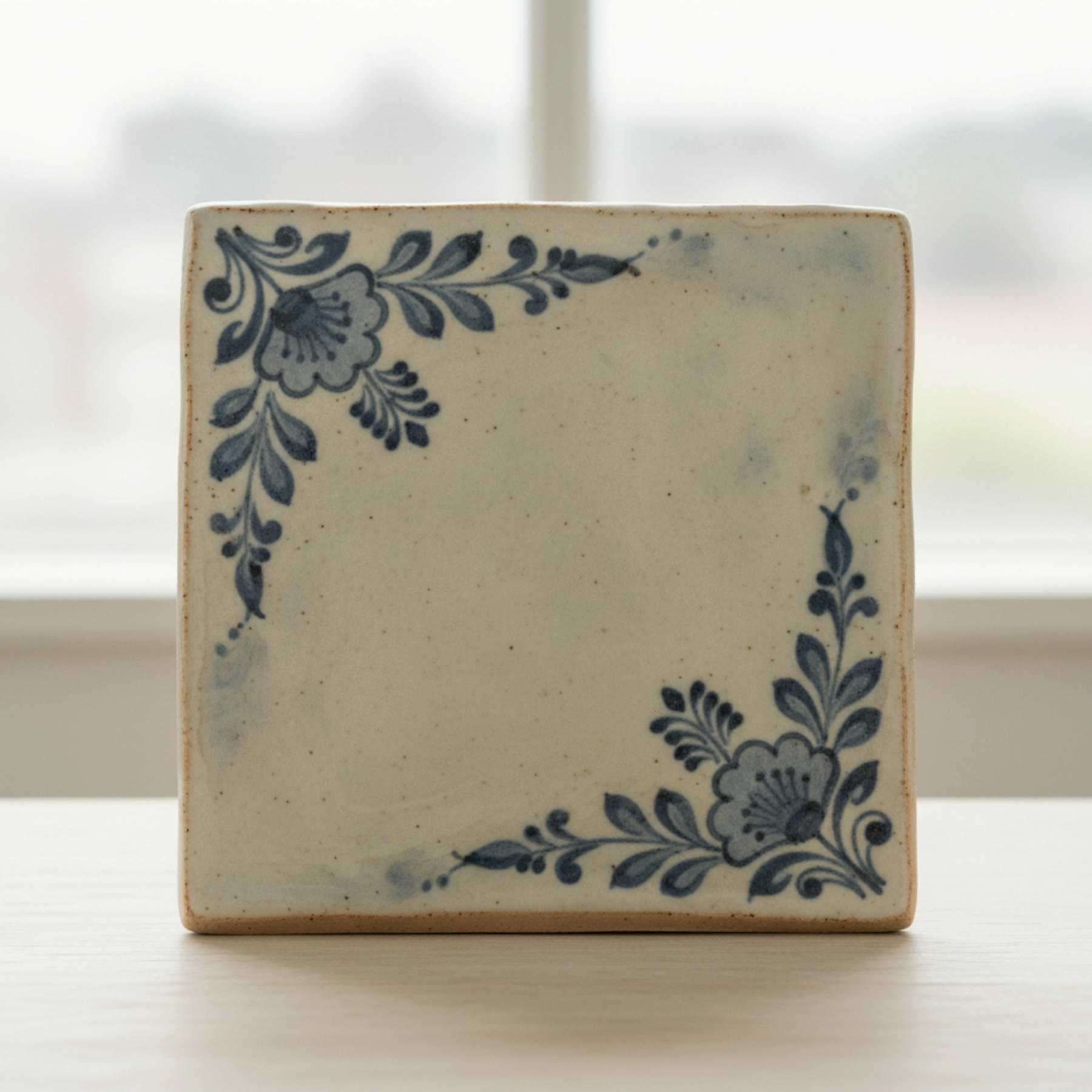 Illustration of a square tile plaque with blue painted floral corners