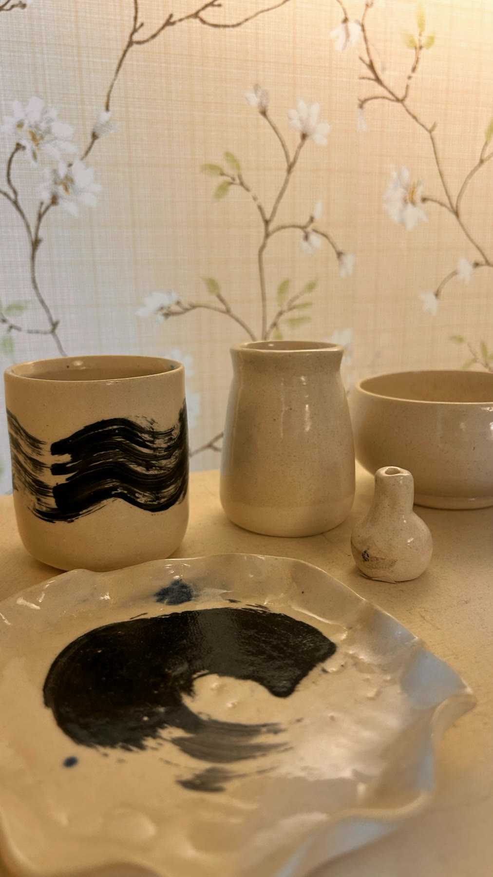 Finished cream cups with dark brushwork beside a vase and a glazed dish