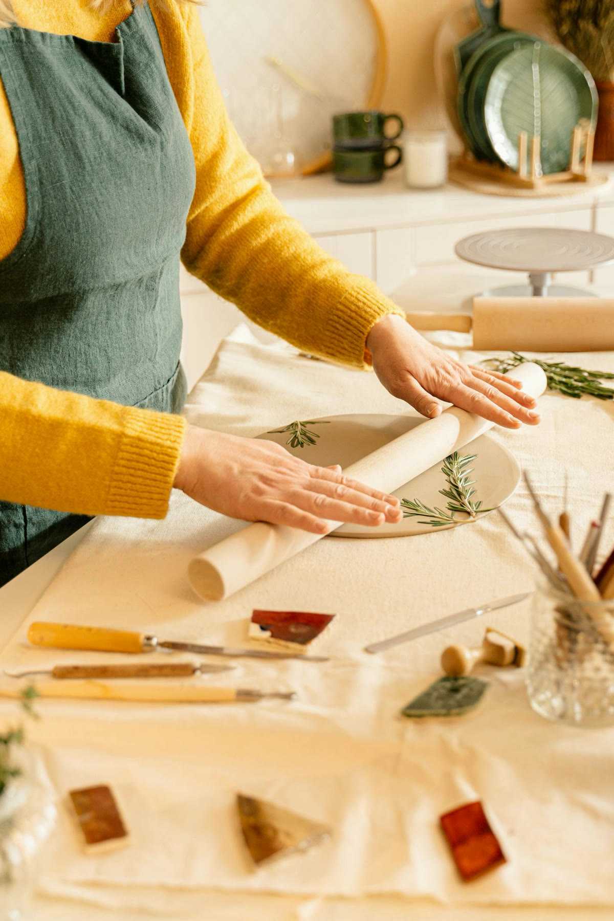 Hands rolling sprigs of leaves into a clay slab on a work table