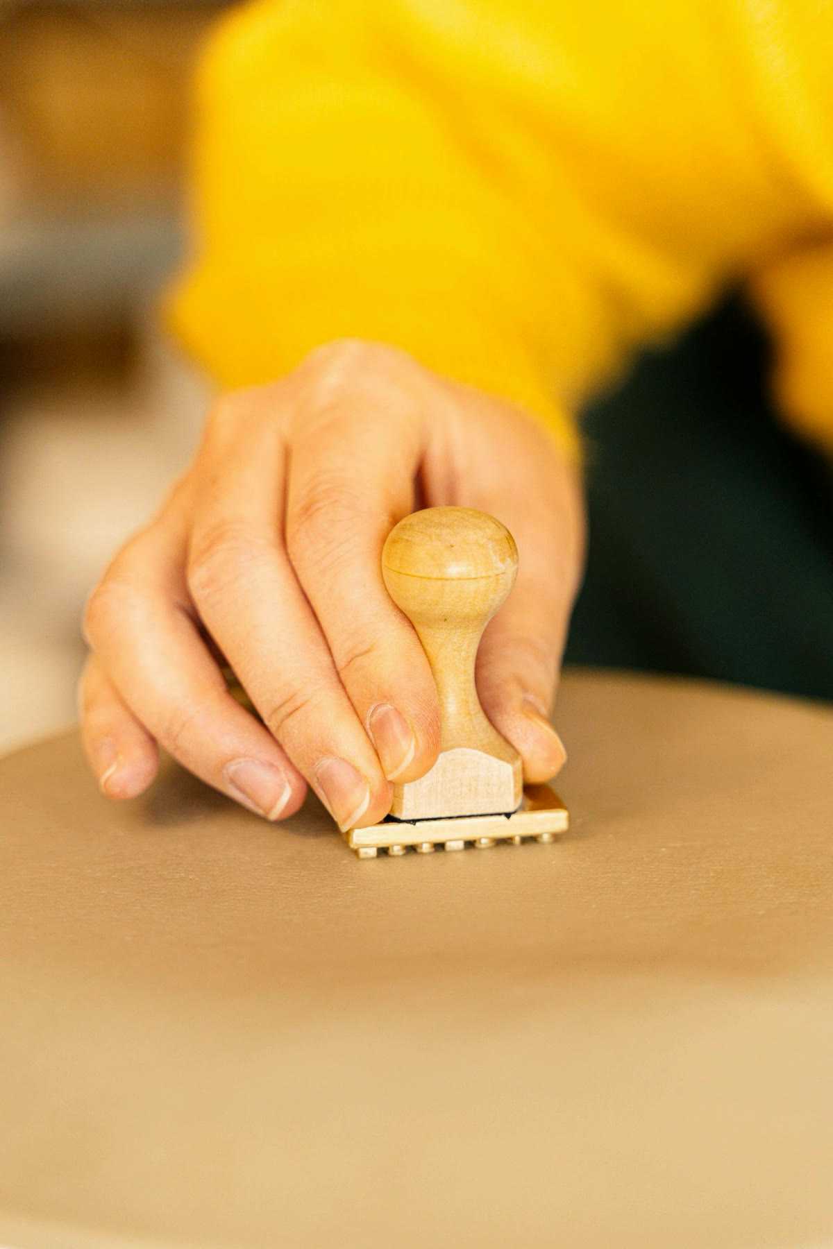 A hand pressing a wooden stamp into soft clay