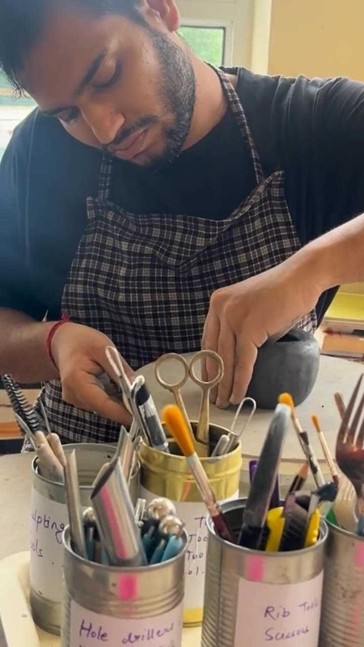 A potter reaching for a modelling tool from labelled tins at the studio bench