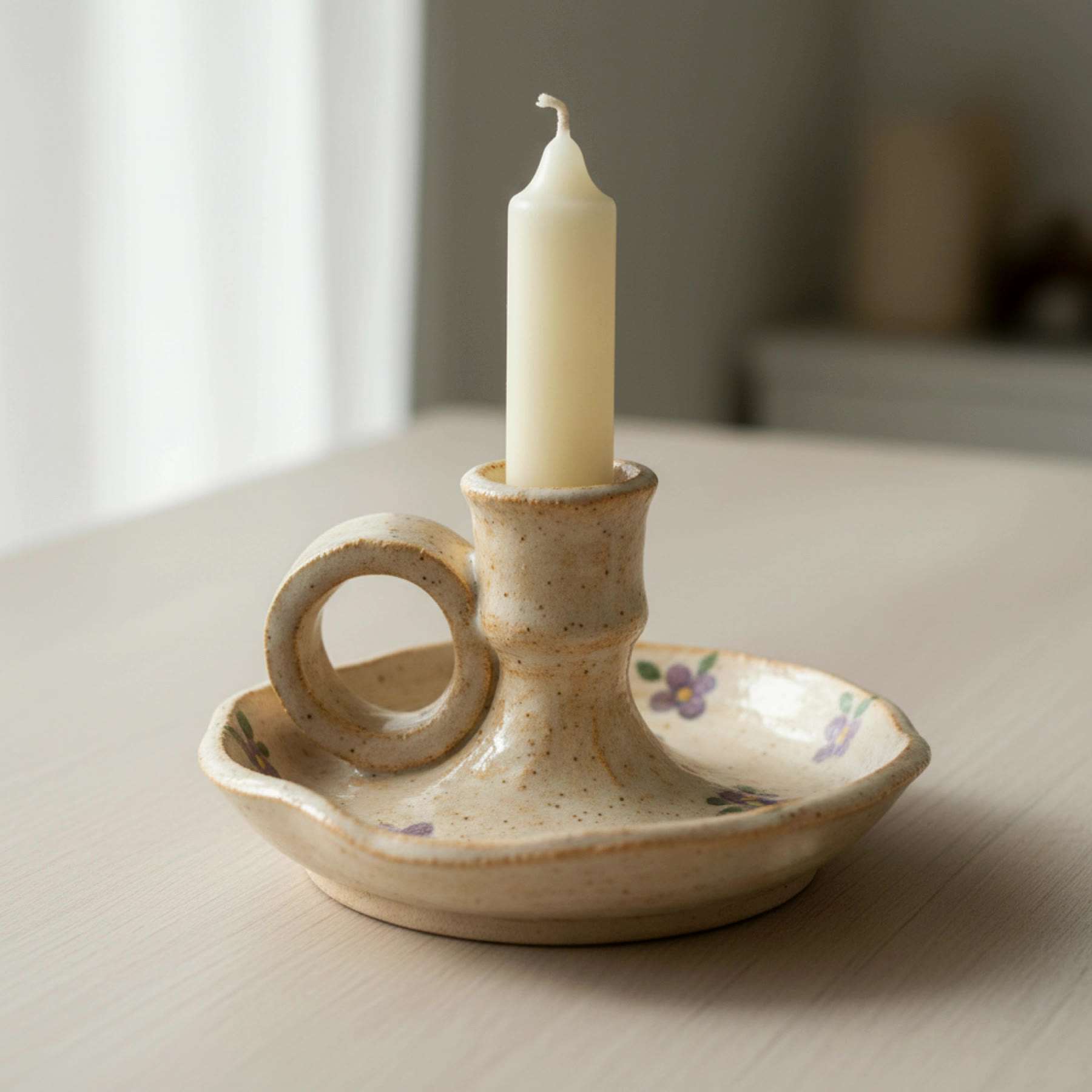 Illustration of a cream chamberstick candle holder with a loop handle and painted flowers