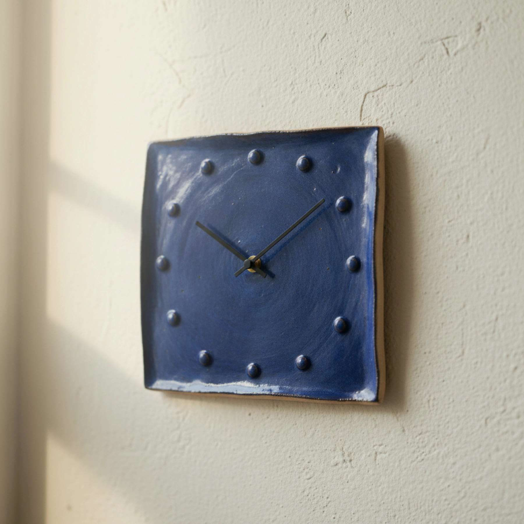 Illustration of an indigo ceramic wall clock with raised dots, hanging on a white wall