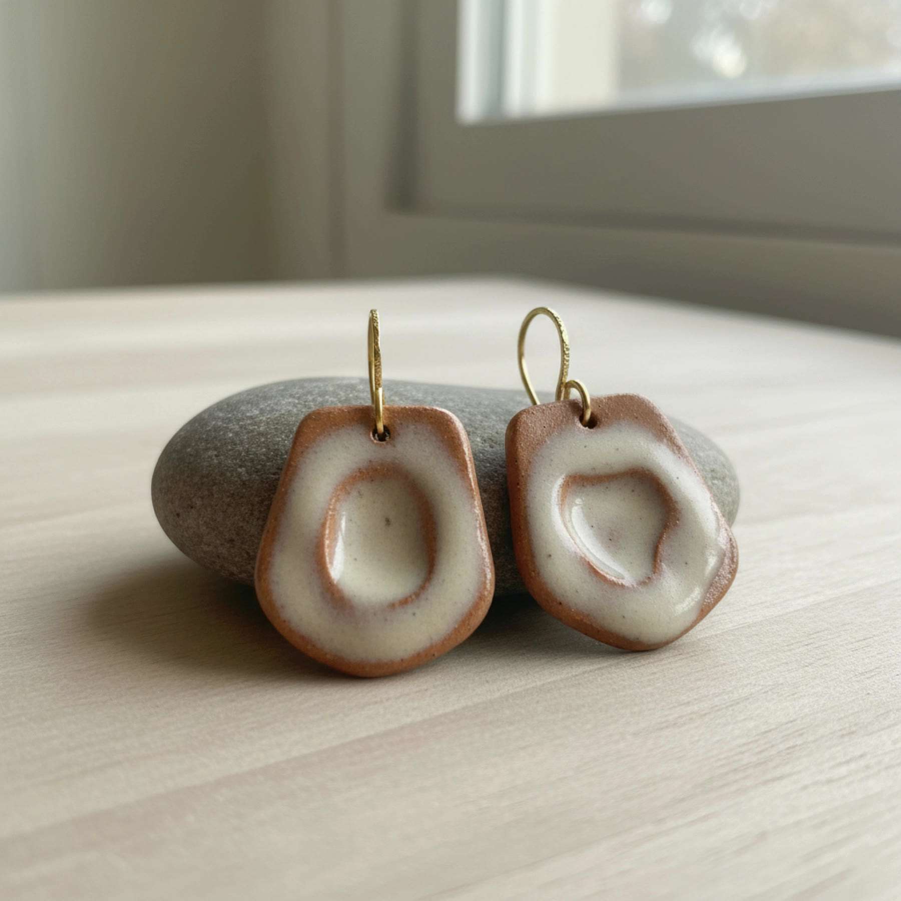 Illustration of a pair of terracotta and cream ceramic drop earrings on a stone