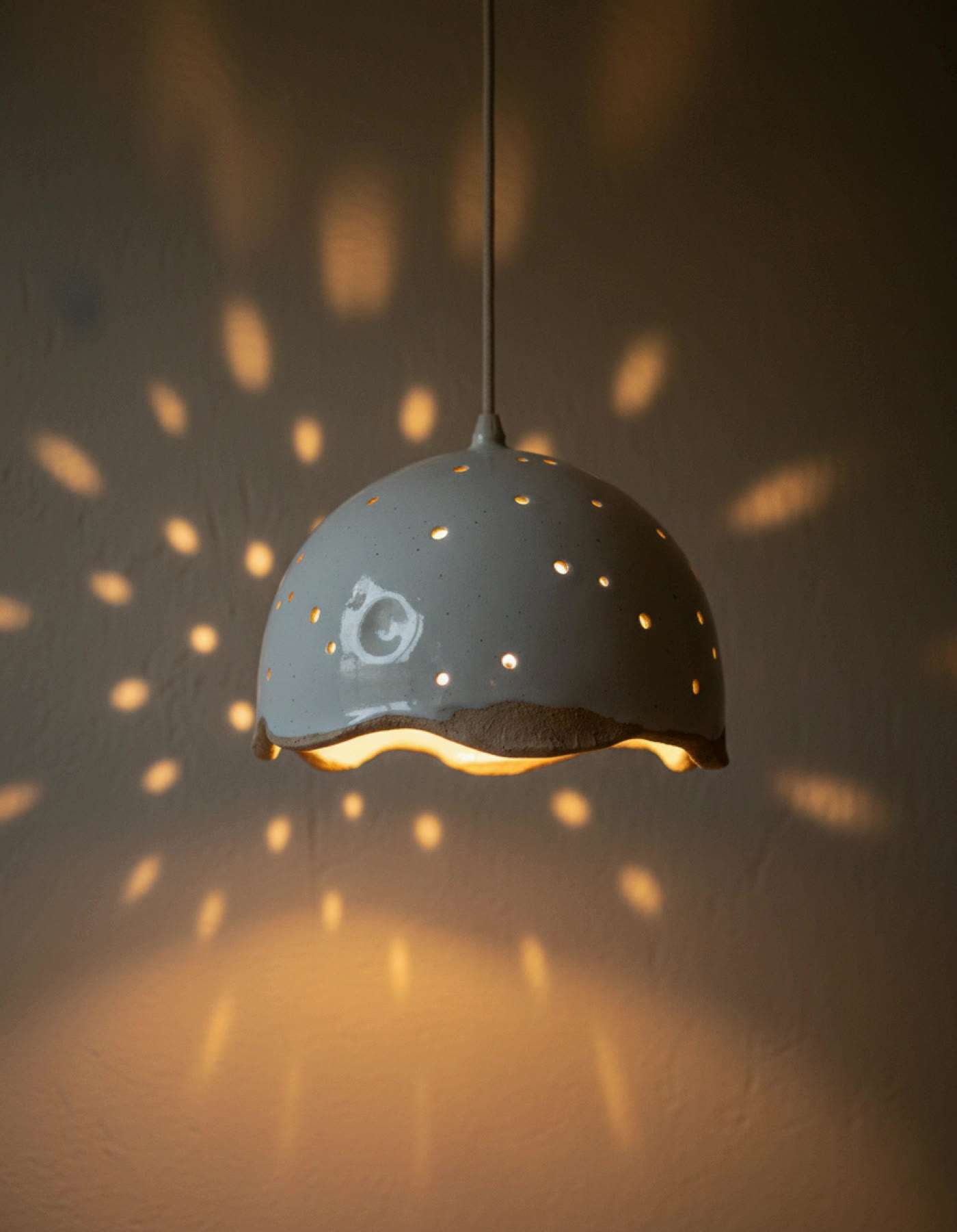 Illustration of a pierced white ceramic pendant lampshade casting dots of light across a wall