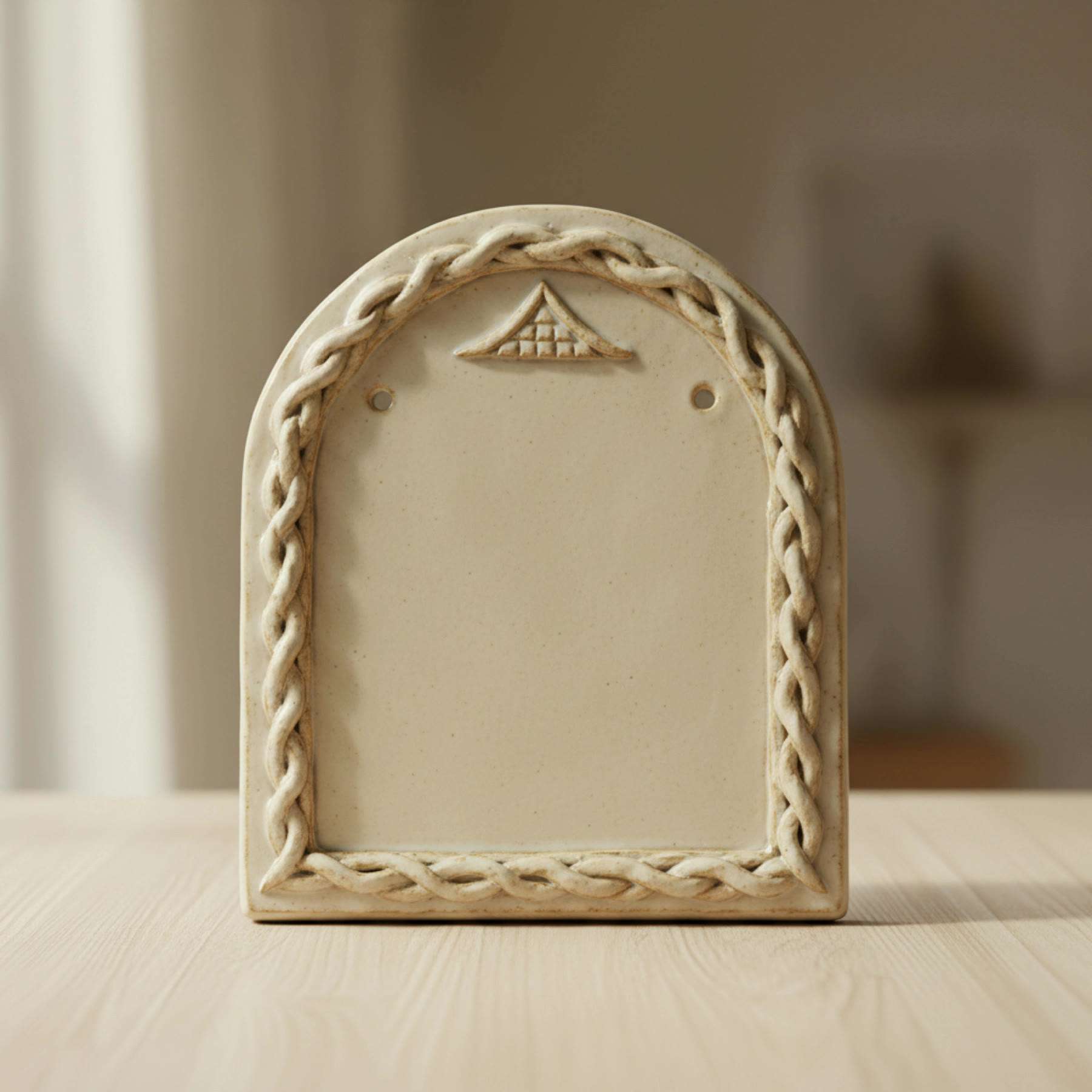 Illustration of an arched cream ceramic plaque with a braided border and a blank centre