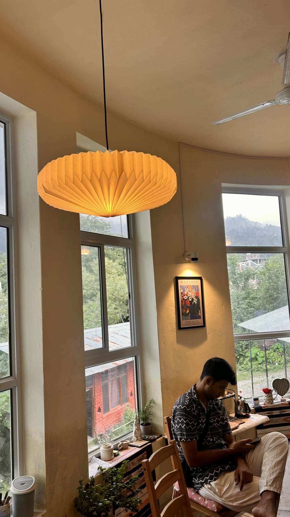 The studio's paper pendant lamp and tall windows, someone working at the far table