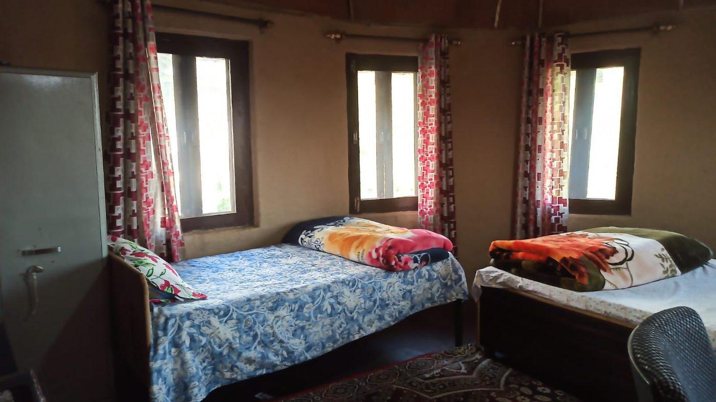 A mud-walled room at the village house with two beds, three windows and a patterned carpet