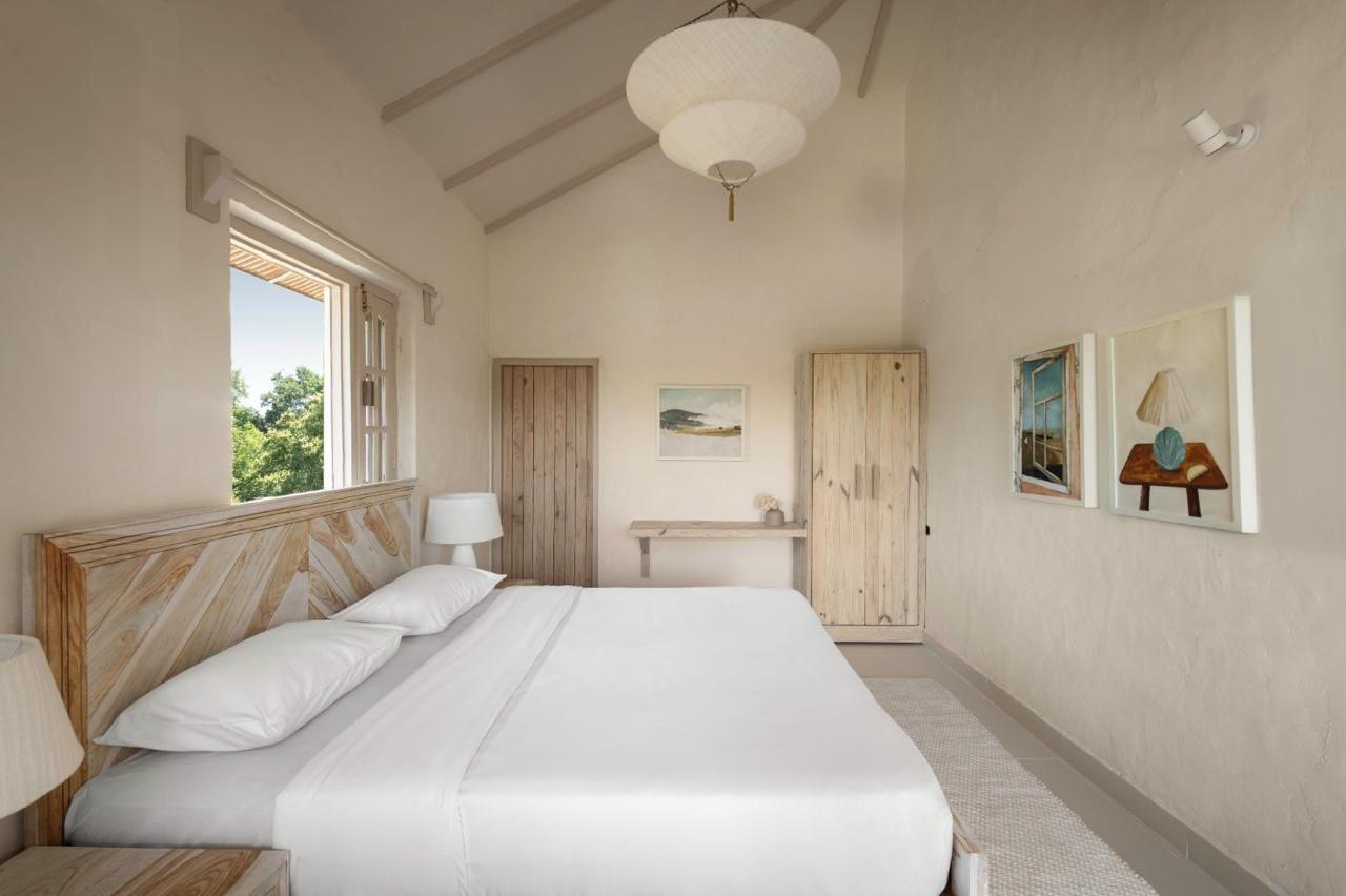 A lime-plastered bedroom with a vaulted ceiling, paper lantern and a window onto trees