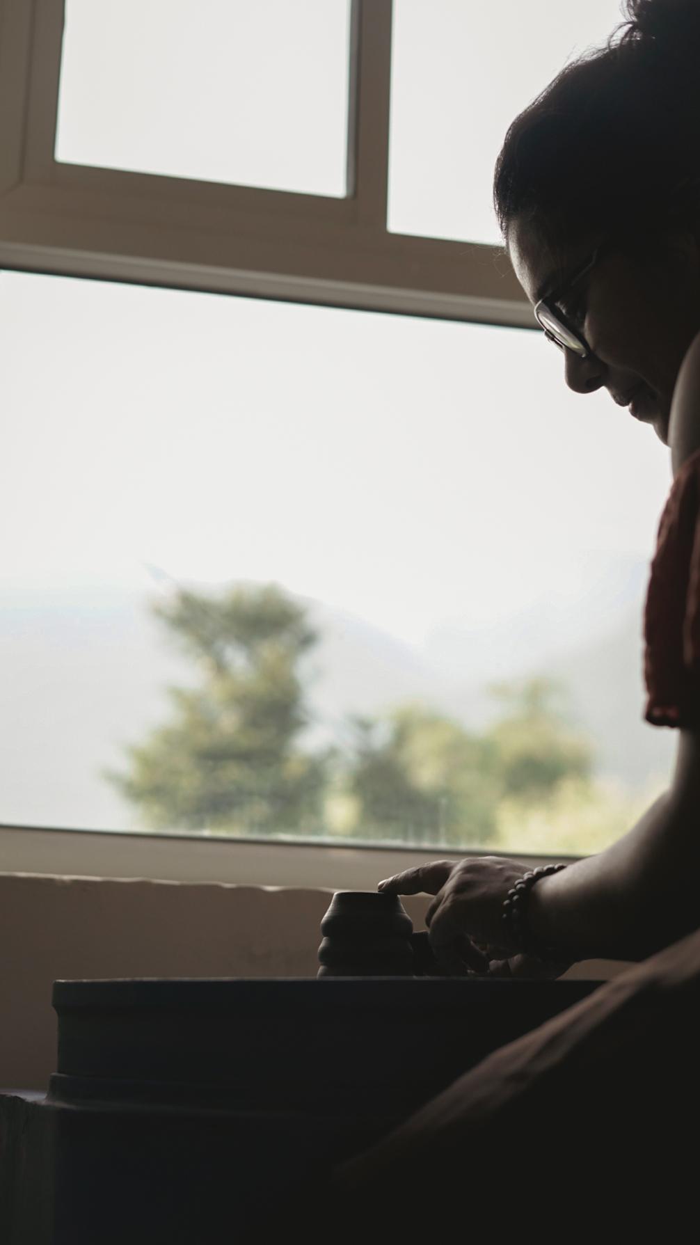 Potter in silhouette at the wheel with Dhauladhar mountains through the studio window
