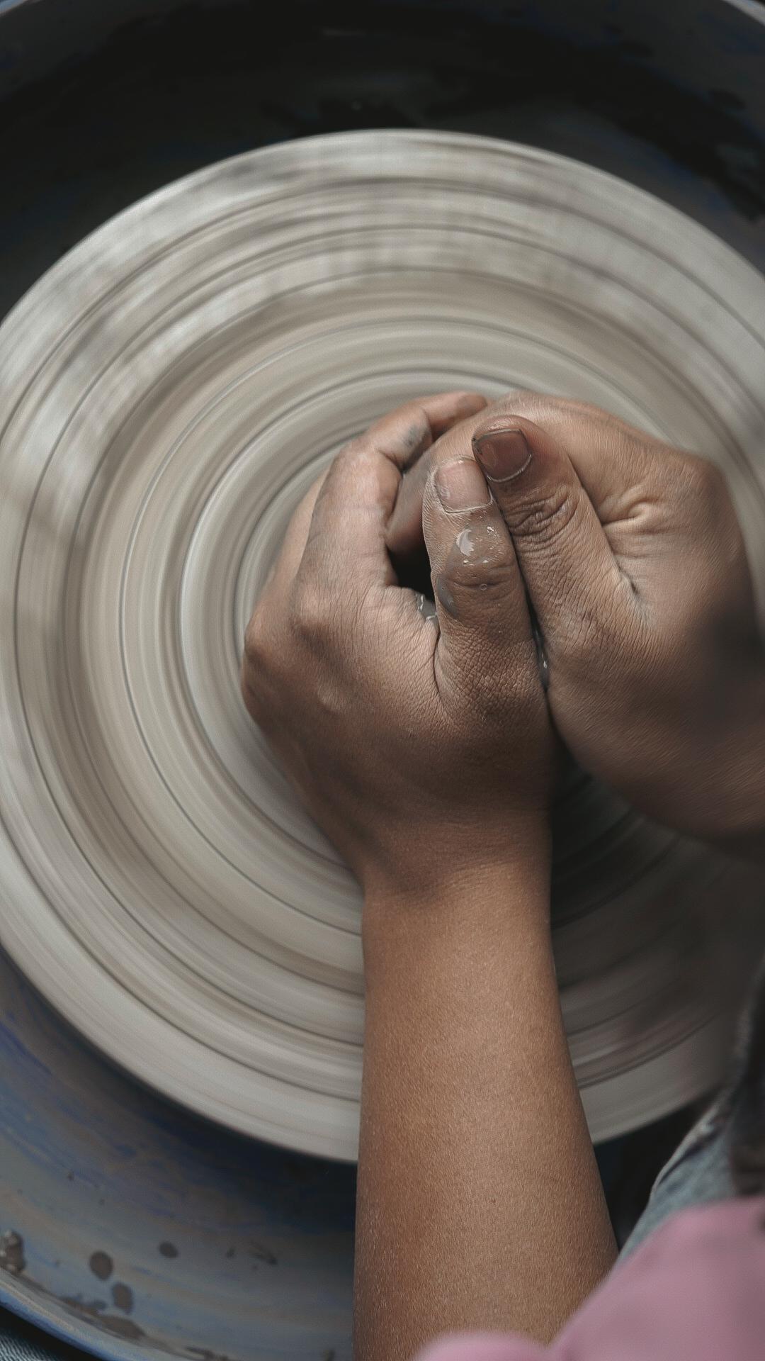 Hands centering wet clay on spinning pottery wheel