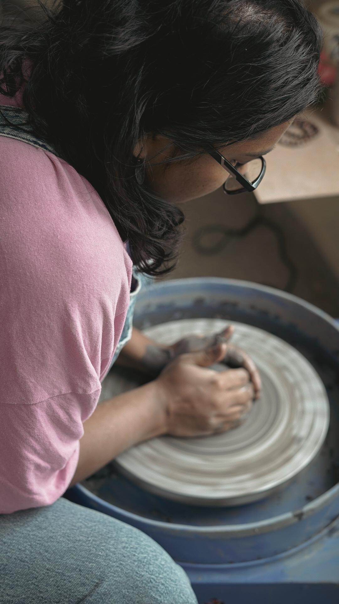 Over-shoulder view of potter shaping clay on the wheel