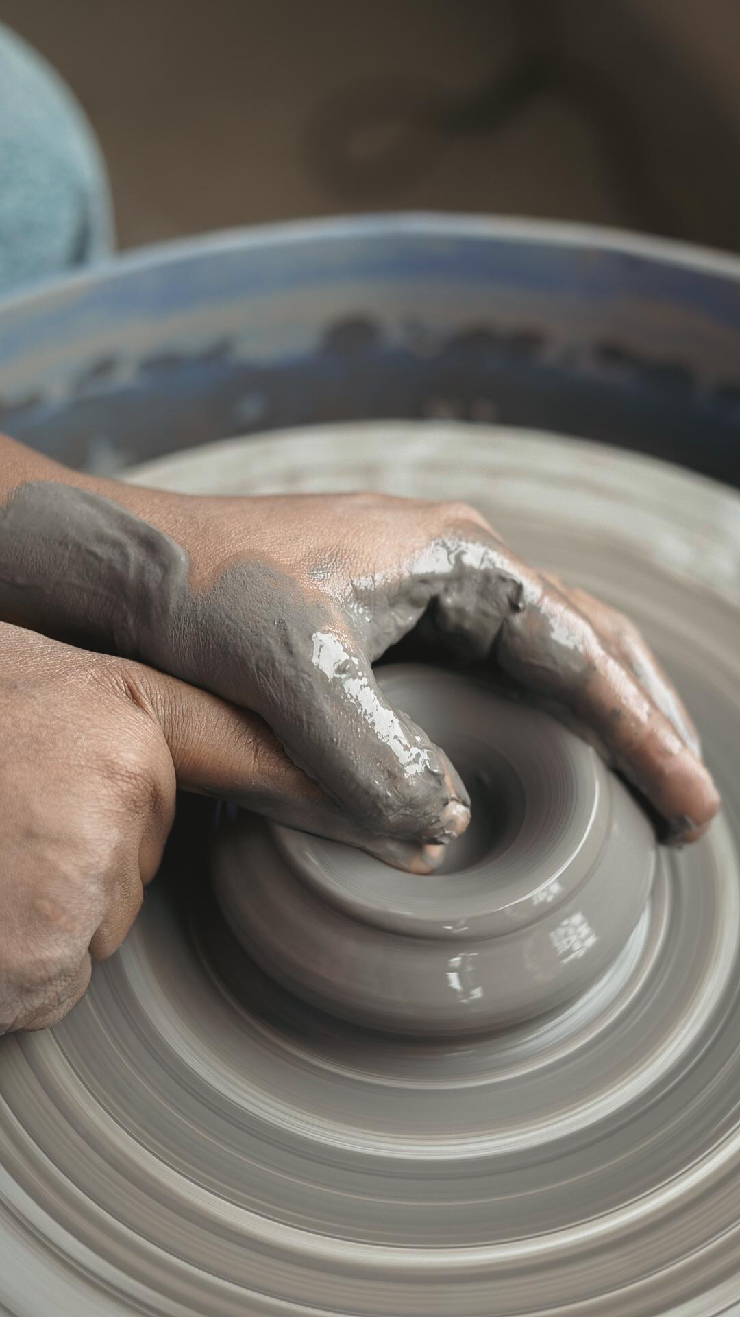 Close-up of clay-covered hands centering clay on pottery wheel