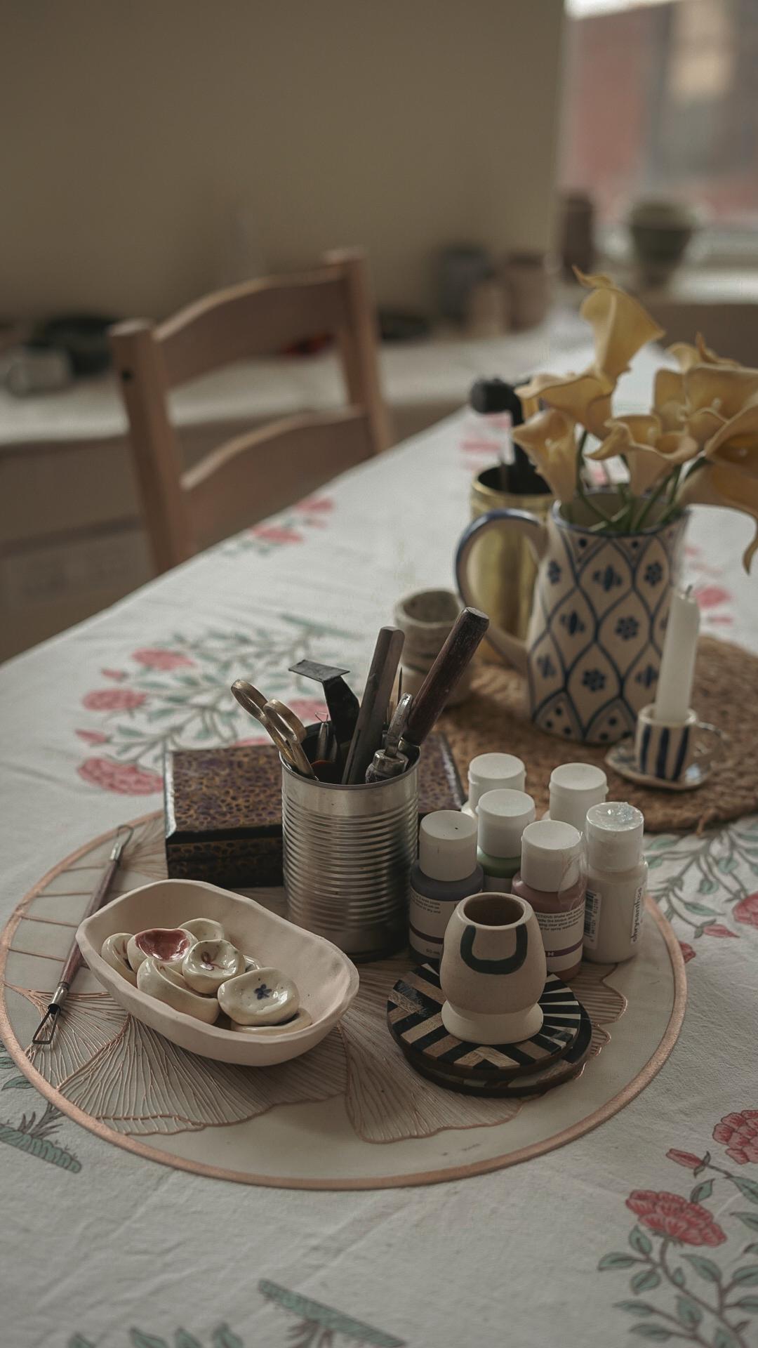 Handmade ceramic pieces and pottery tools on floral tablecloth