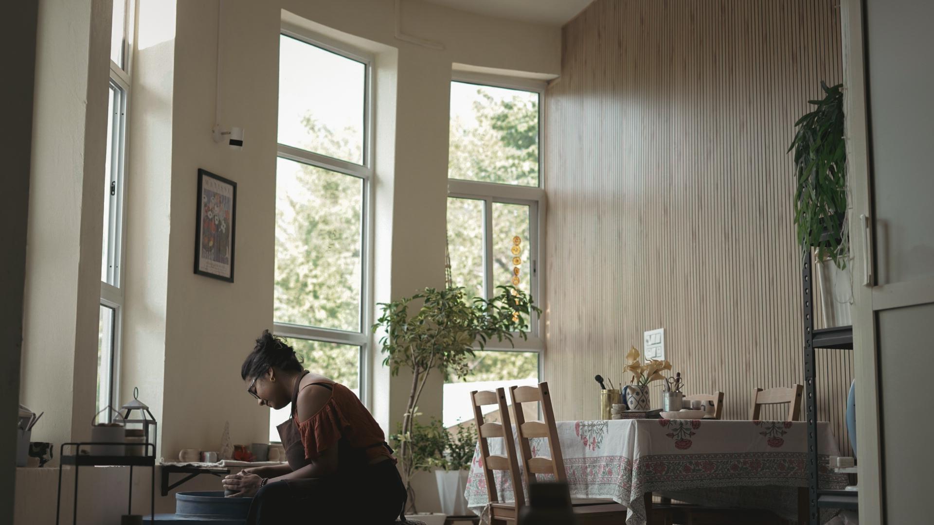 The studio's one room — tall windows down one side, someone working at a table, and the long dining table laid at the far end