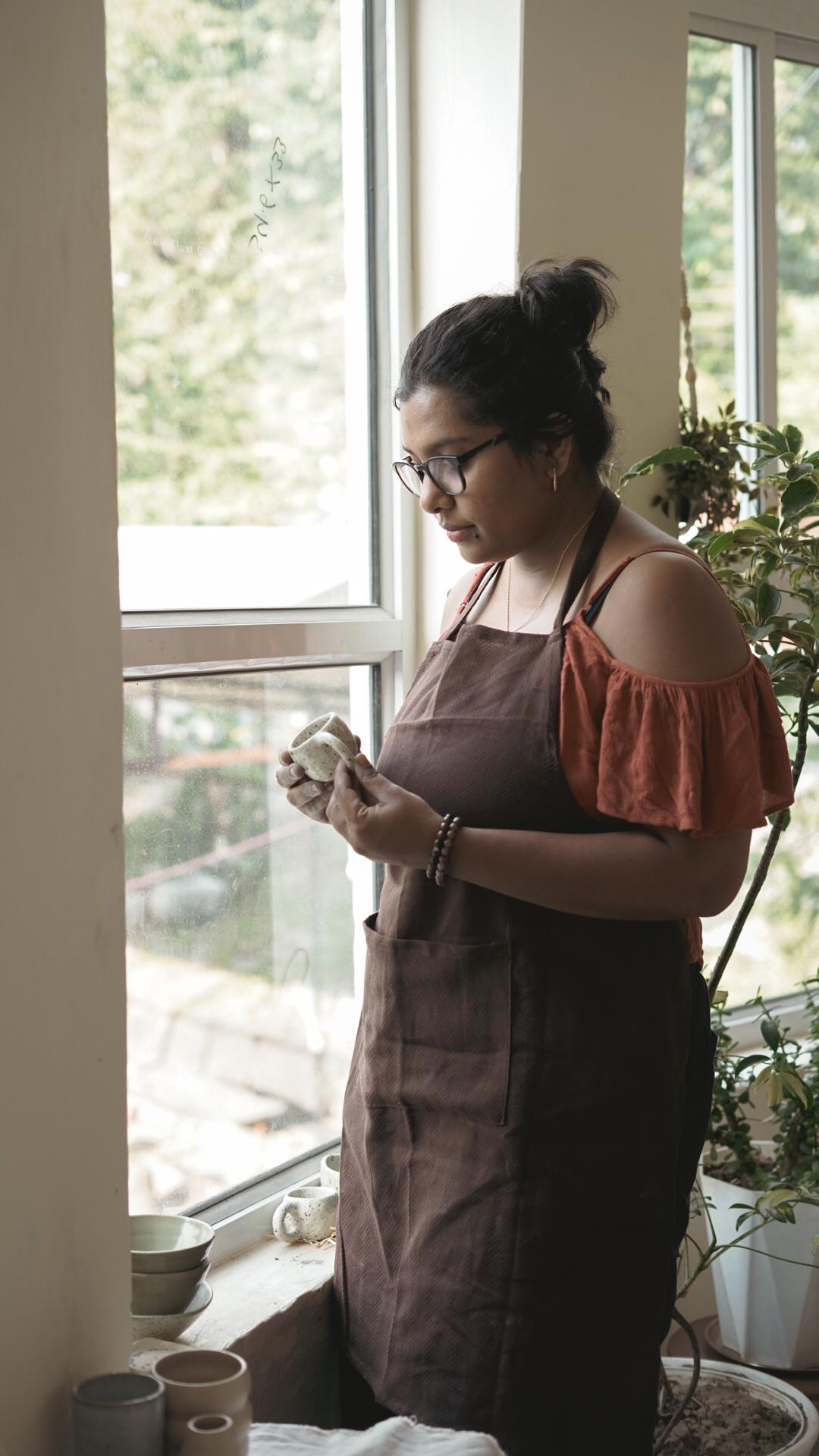 Madhumita Chatterjee inspecting a handmade speckled ceramic mug by the studio window