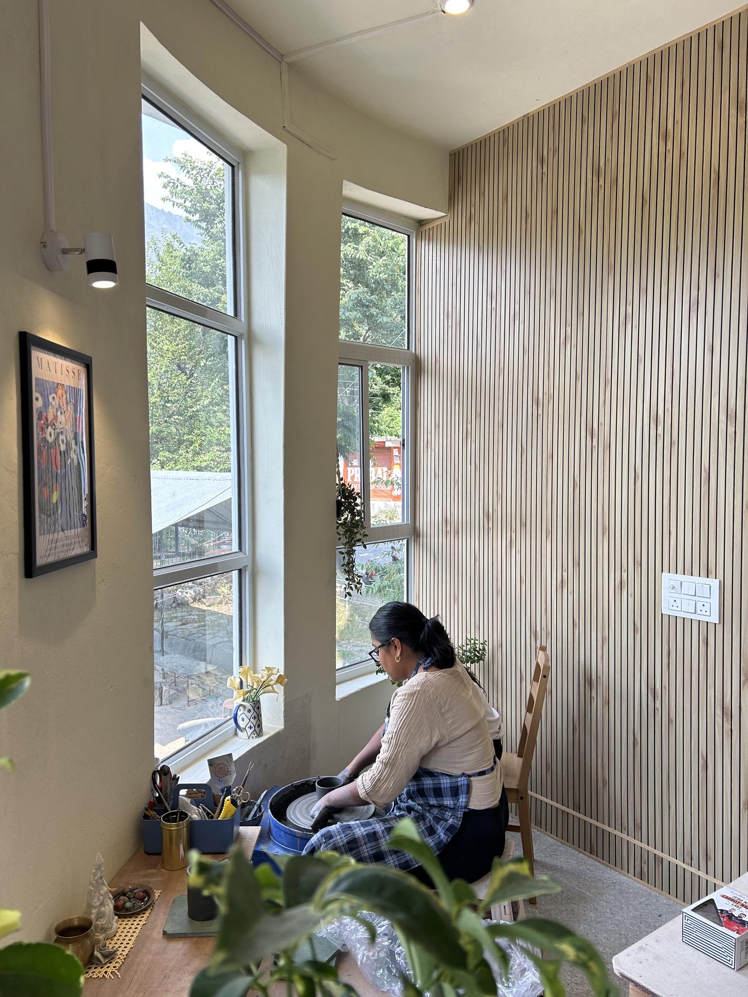 Mita at the pottery wheel by tall windows with mountain view