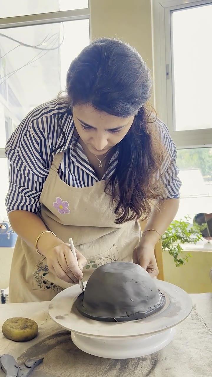 Madhumita carving fine lines into a dark clay dome turning on a banding wheel