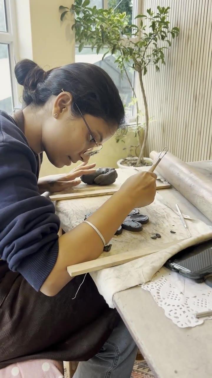 Two people working side by side at the table, one incising fine detail into a clay piece