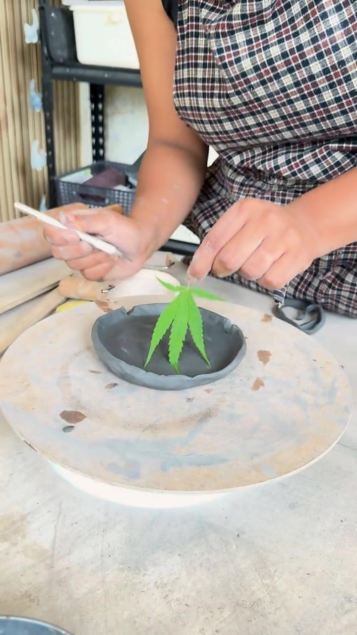 Hands pressing a fresh leaf into a dark clay dish with a wooden tool