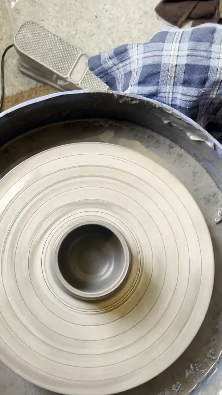 Clay-covered hands opening a cylinder on a spinning wheel, seen from above