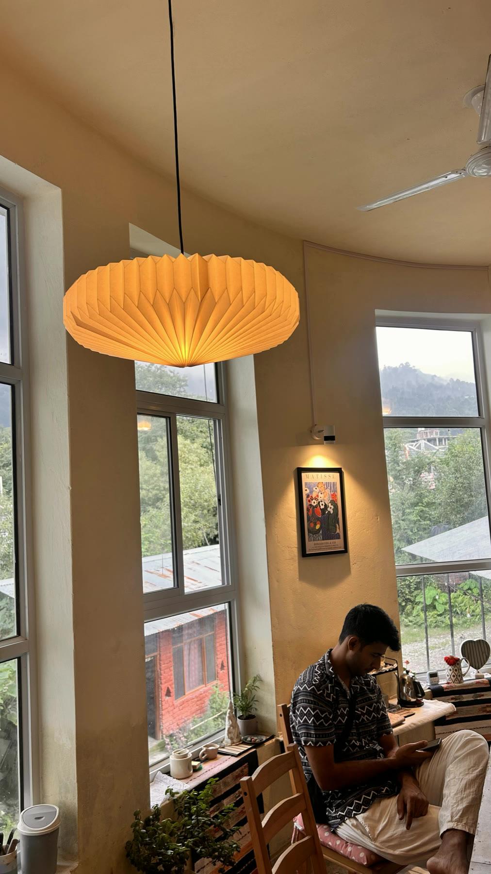 The studio's paper pendant lamp and full-height windows, someone working alone at the far table