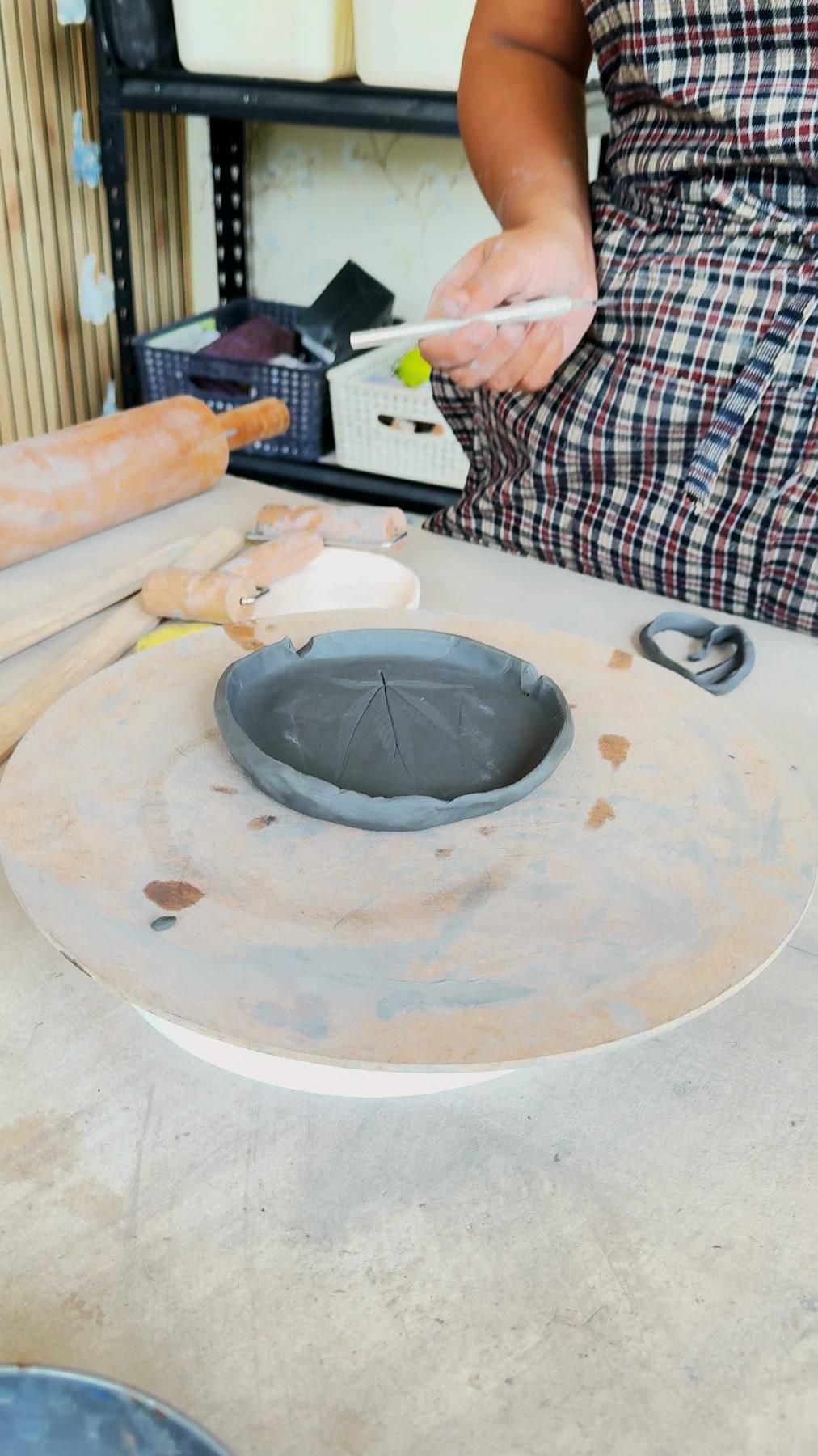 Hands lifting a pressed leaf away from a dark clay dish, its veins left in the surface