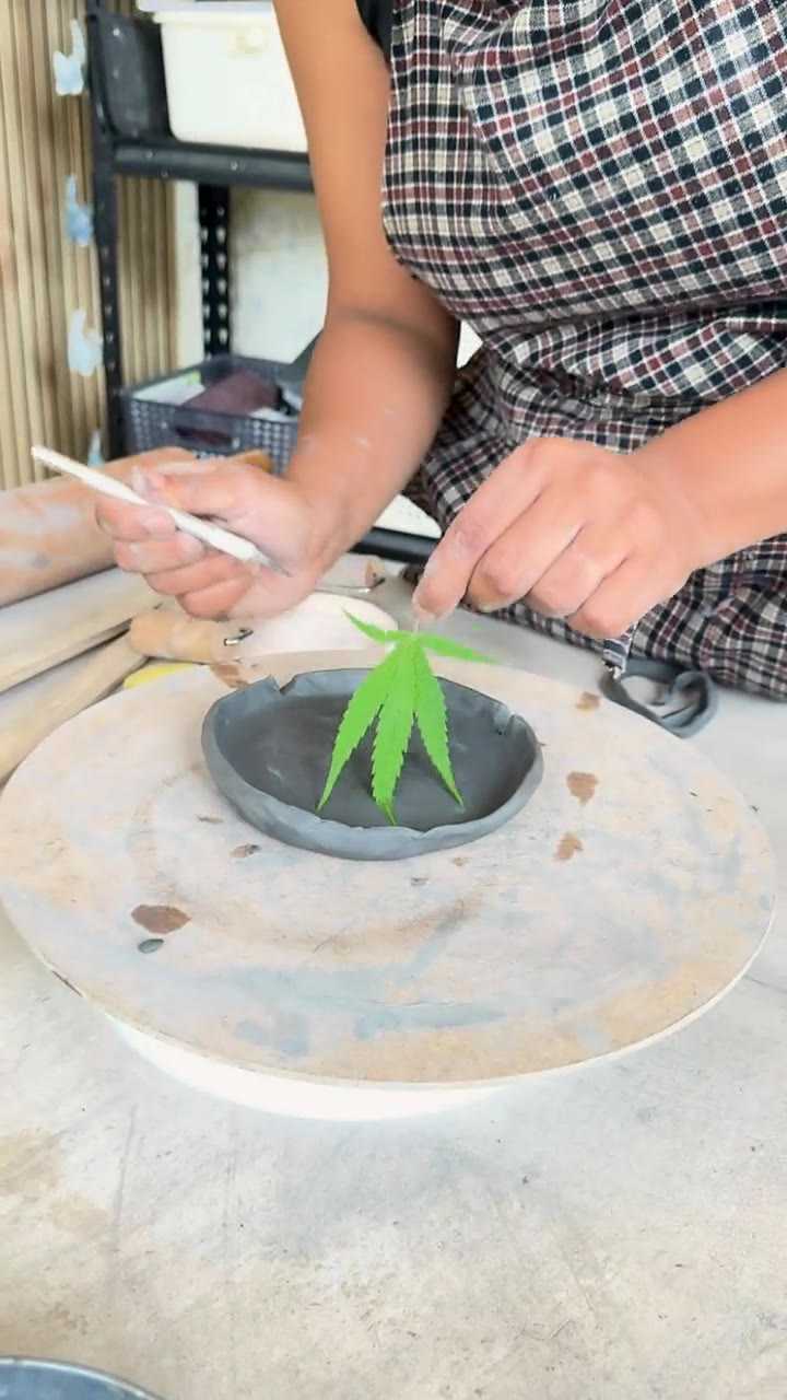 Hands pressing a fresh leaf into a dark clay dish with a wooden tool