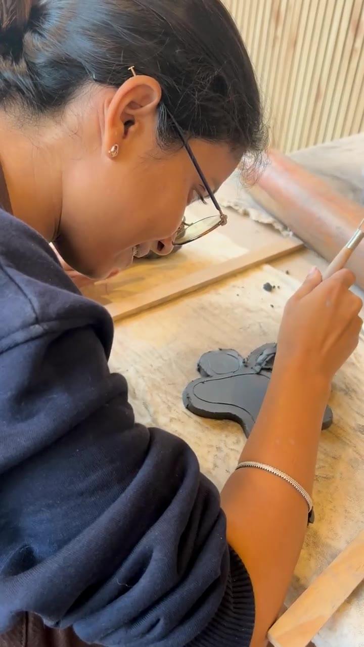 A needle tool cutting a petal shape out of a dark clay slab