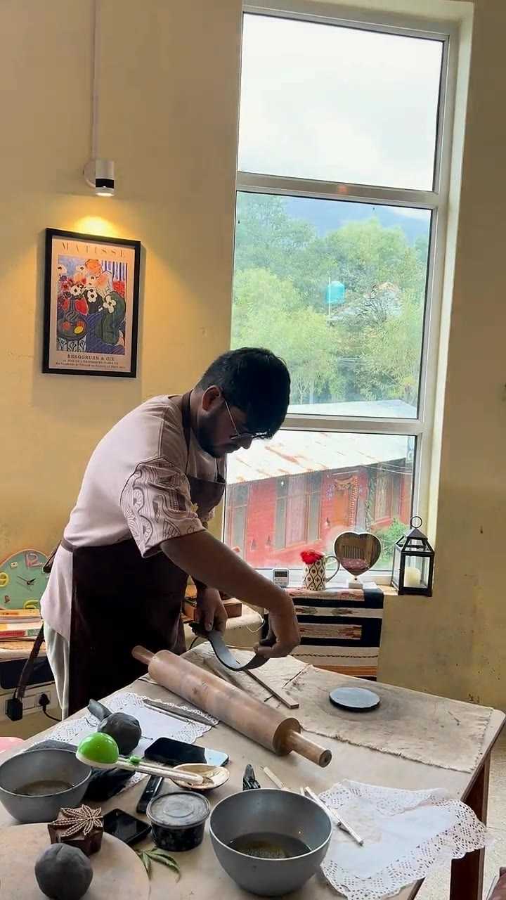 A guest rolling out a clay slab with a wooden pin at the window table