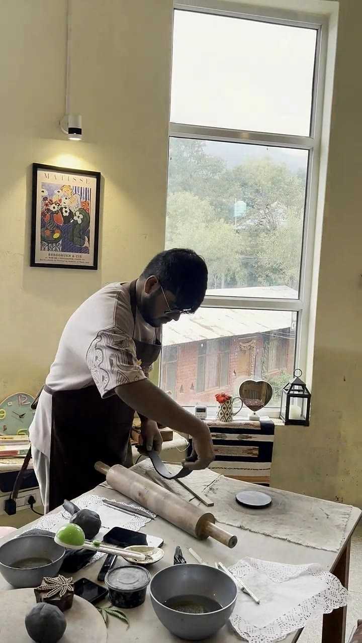 A guest rolling out a clay slab with a wooden pin at the window table