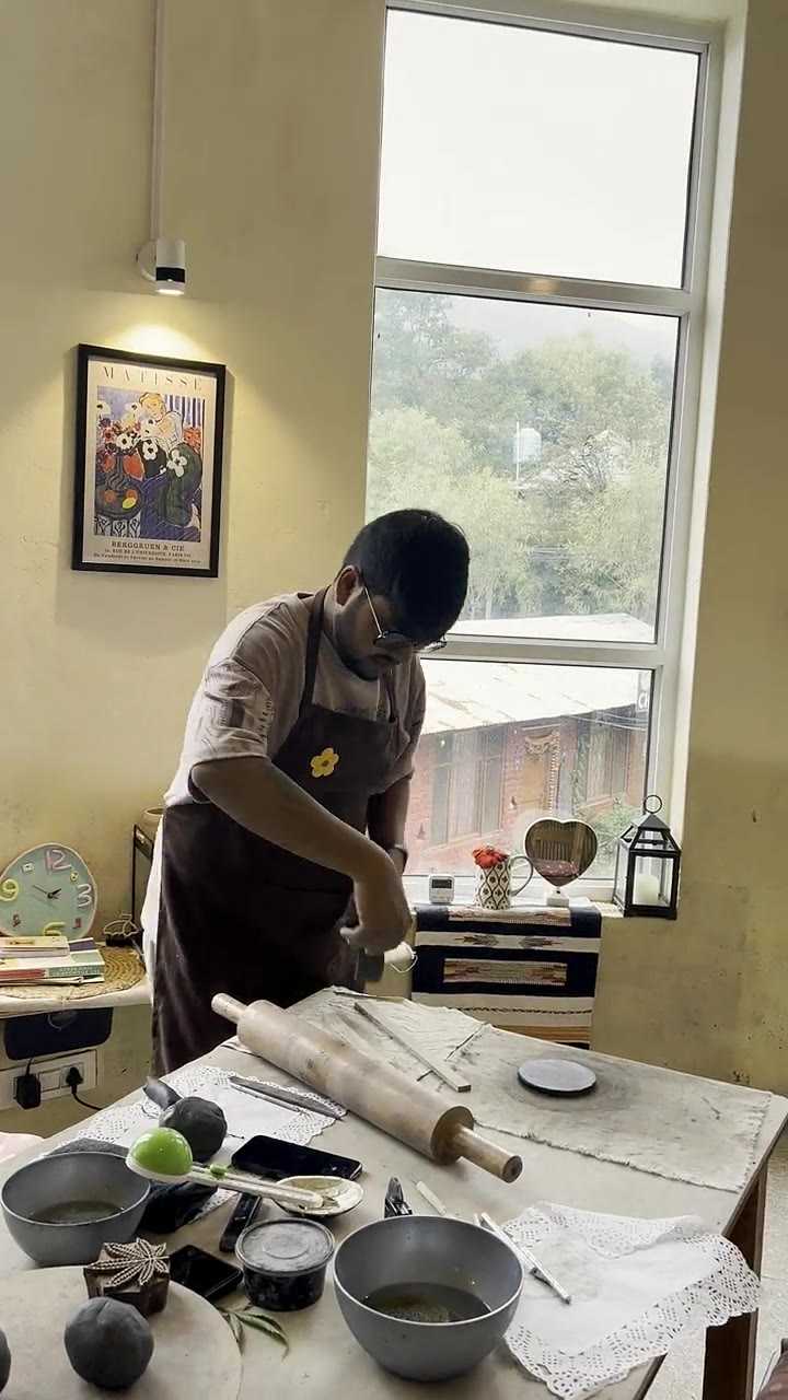 A guest rolling out a clay slab with a wooden pin at the studio's window table