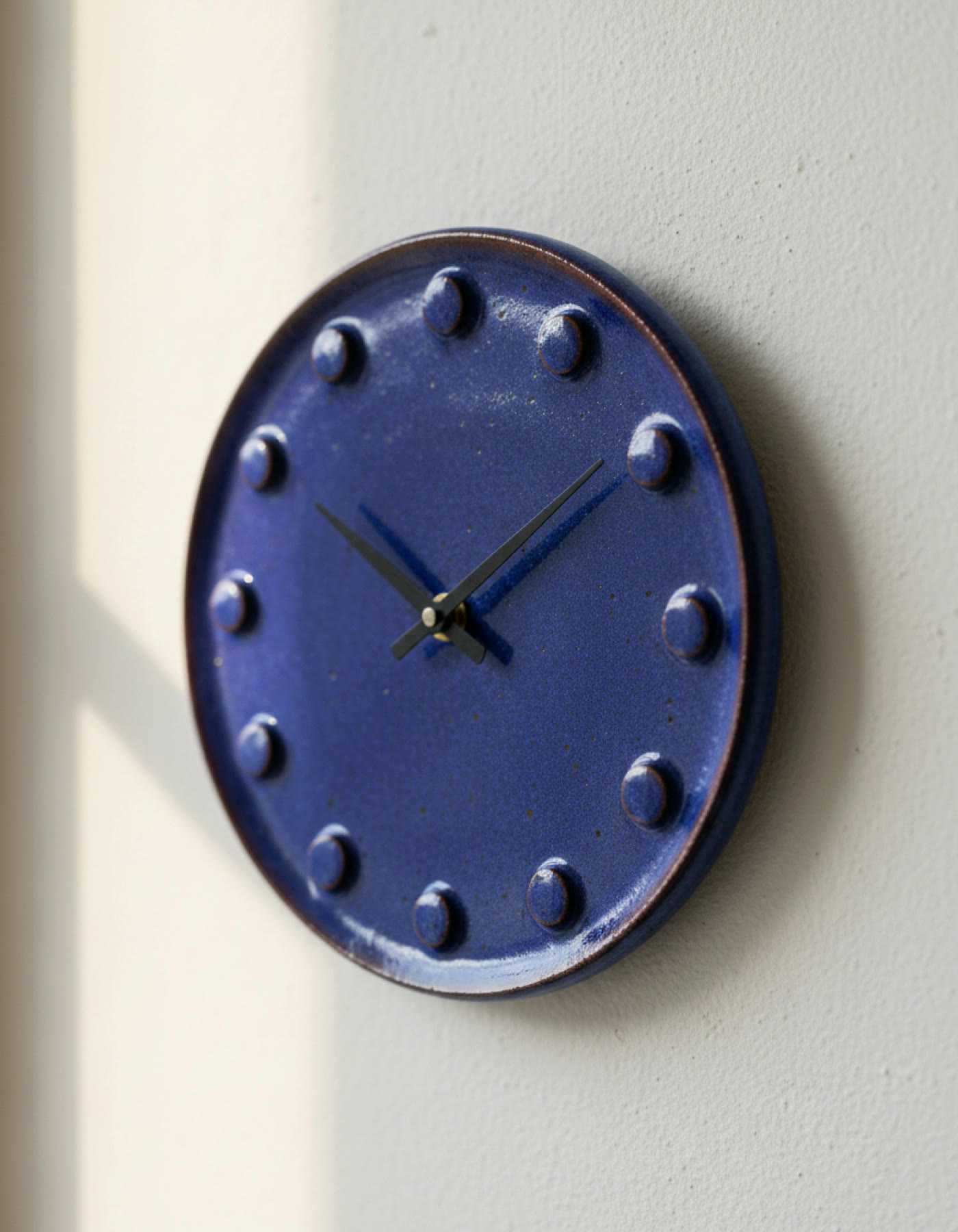 Illustration of a round indigo ceramic wall clock with raised dots for the hours