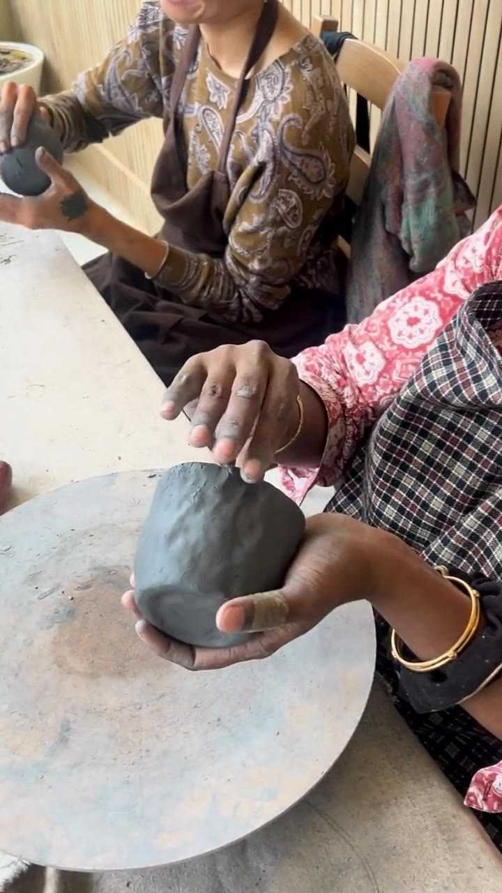 Two pairs of hands pressing a ball of grey clay on a plaster bat