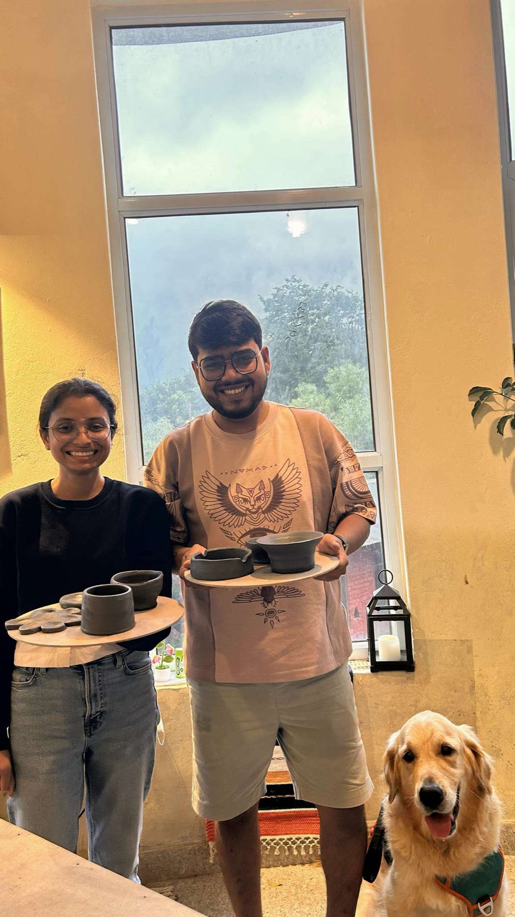 Two guests holding a board of finished cups and bowls they made