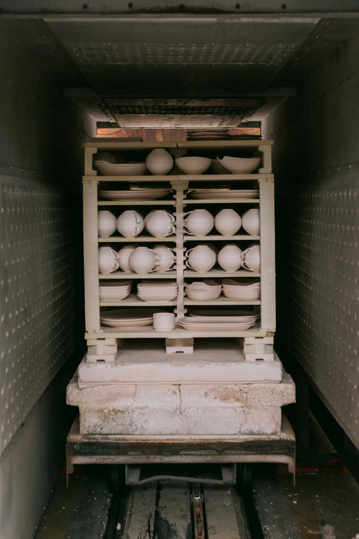 Unglazed cups and dishes stacked on shelves inside a kiln