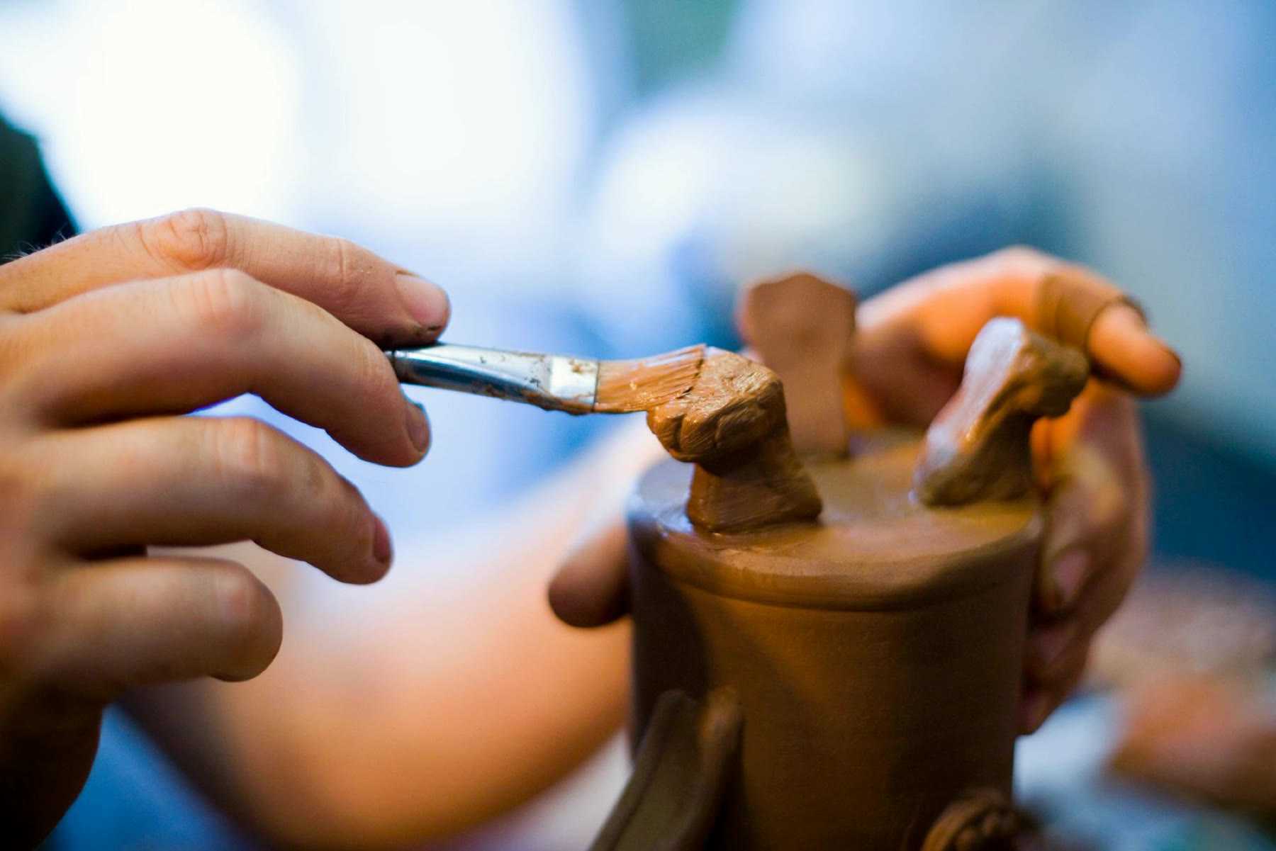 Hands holding a fine brush to paint a small ceramic piece