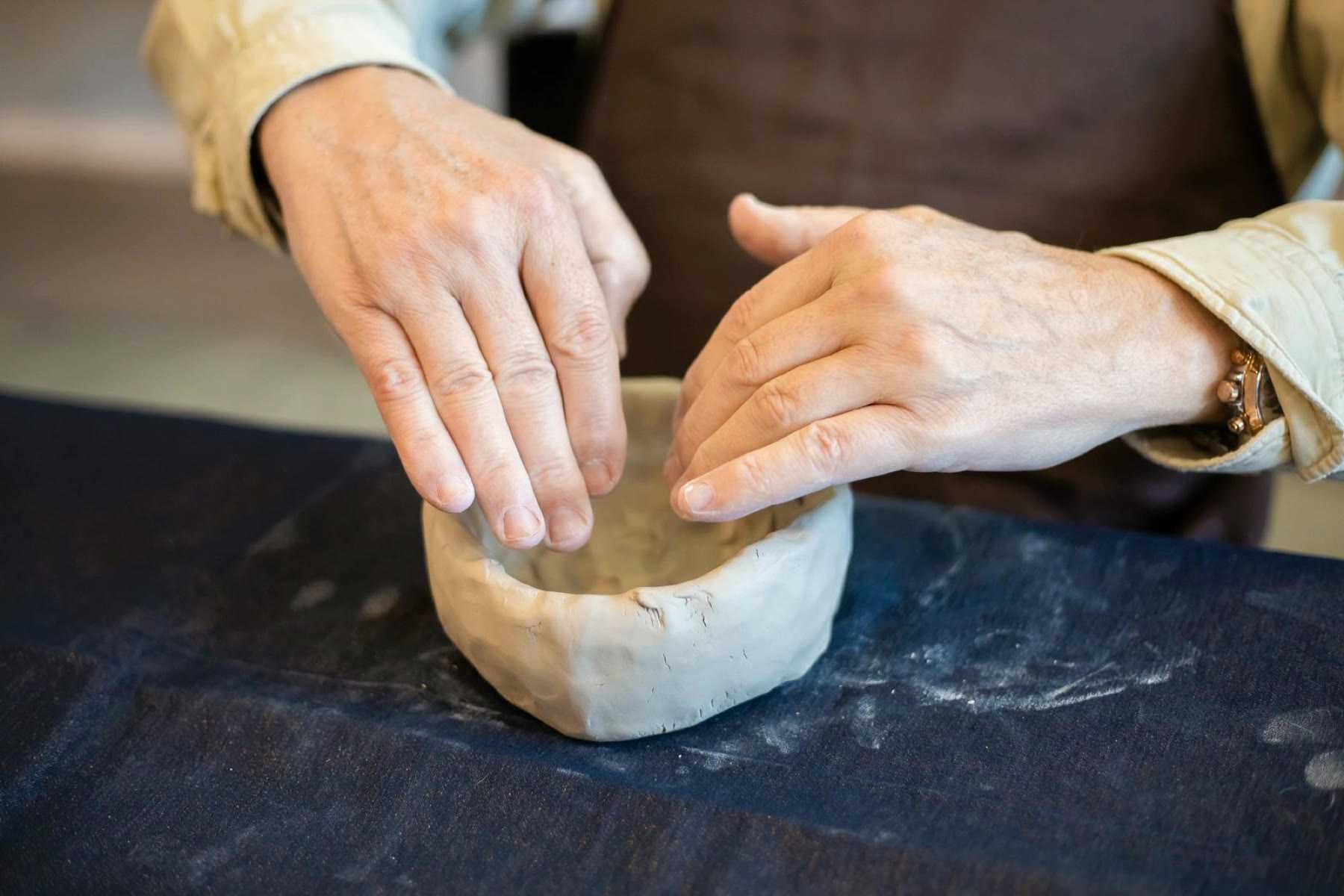 Two hands pinching the wall of a small clay bowl