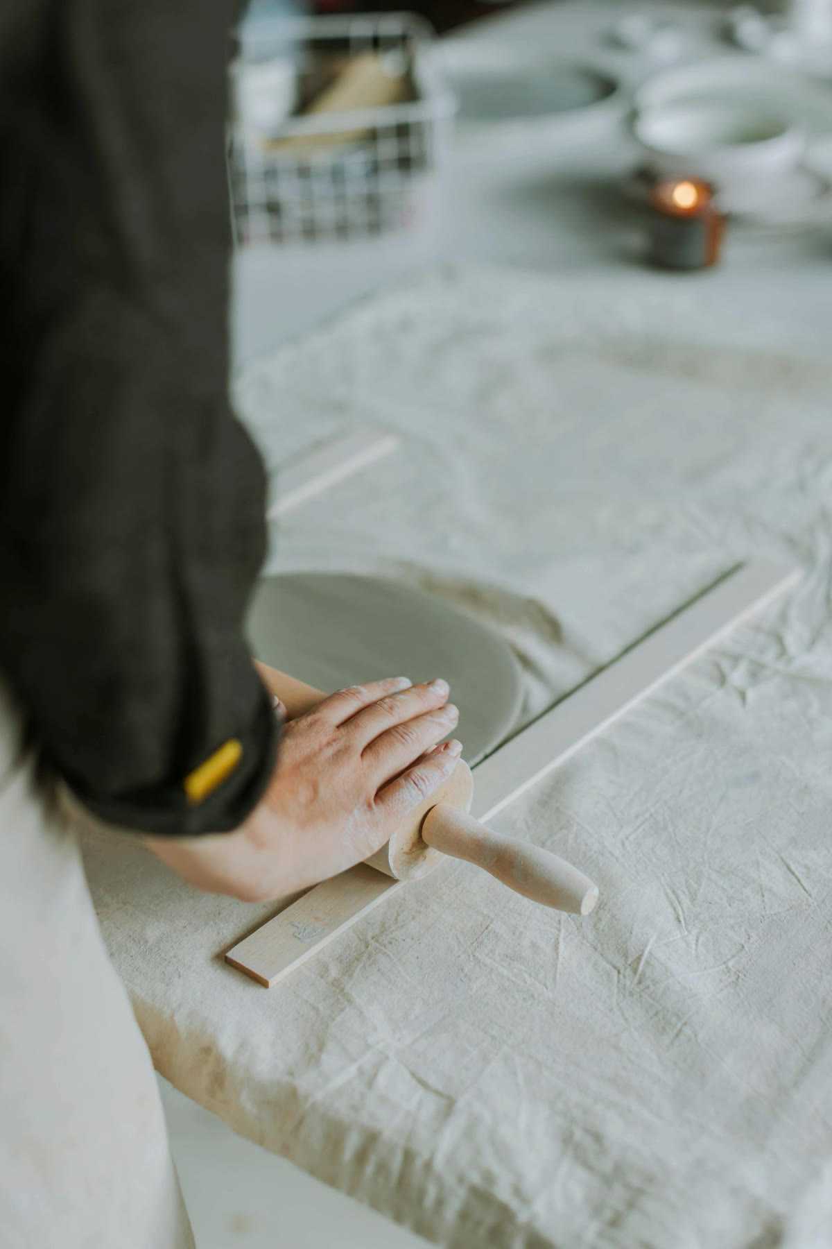 Hands rolling clay flat with a wooden rolling pin