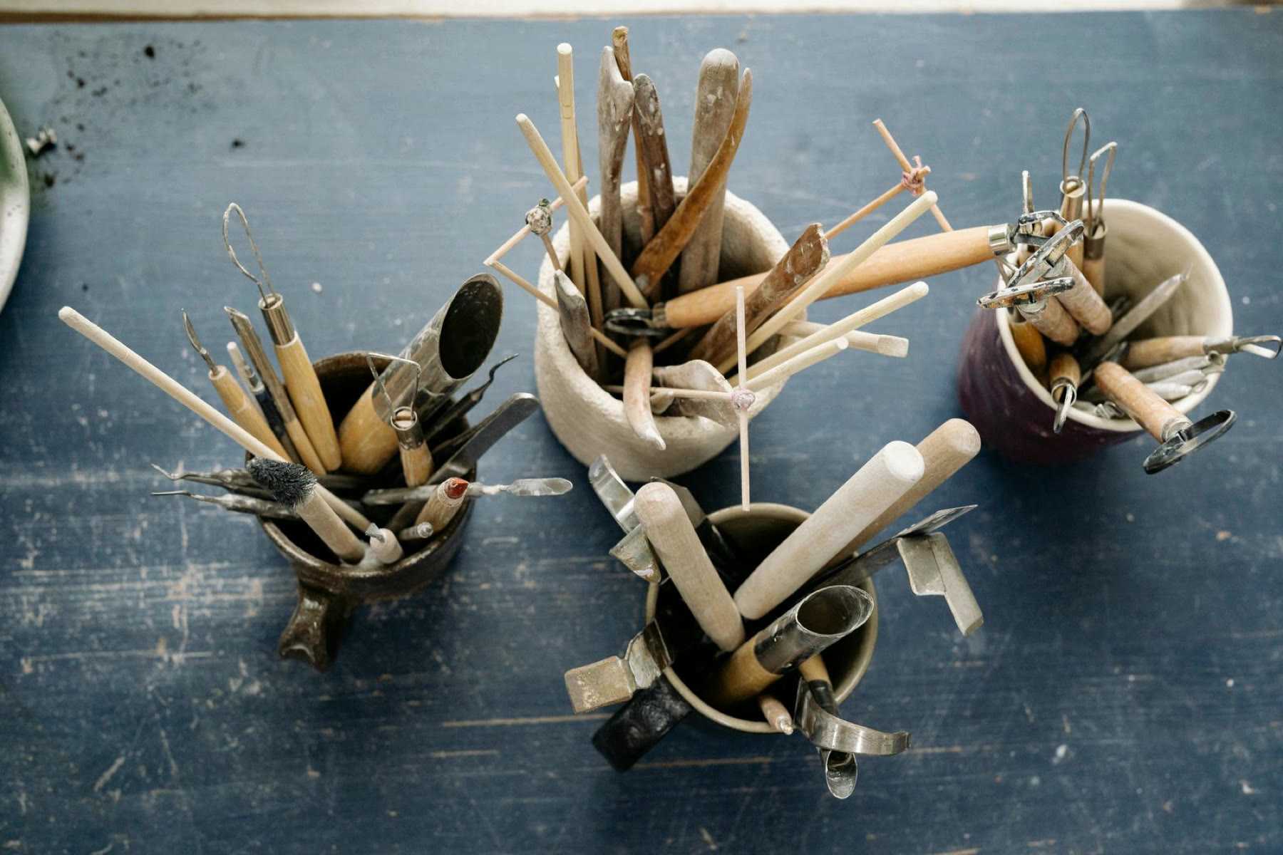 Pottery modelling tools standing in mugs on a blue table, from above