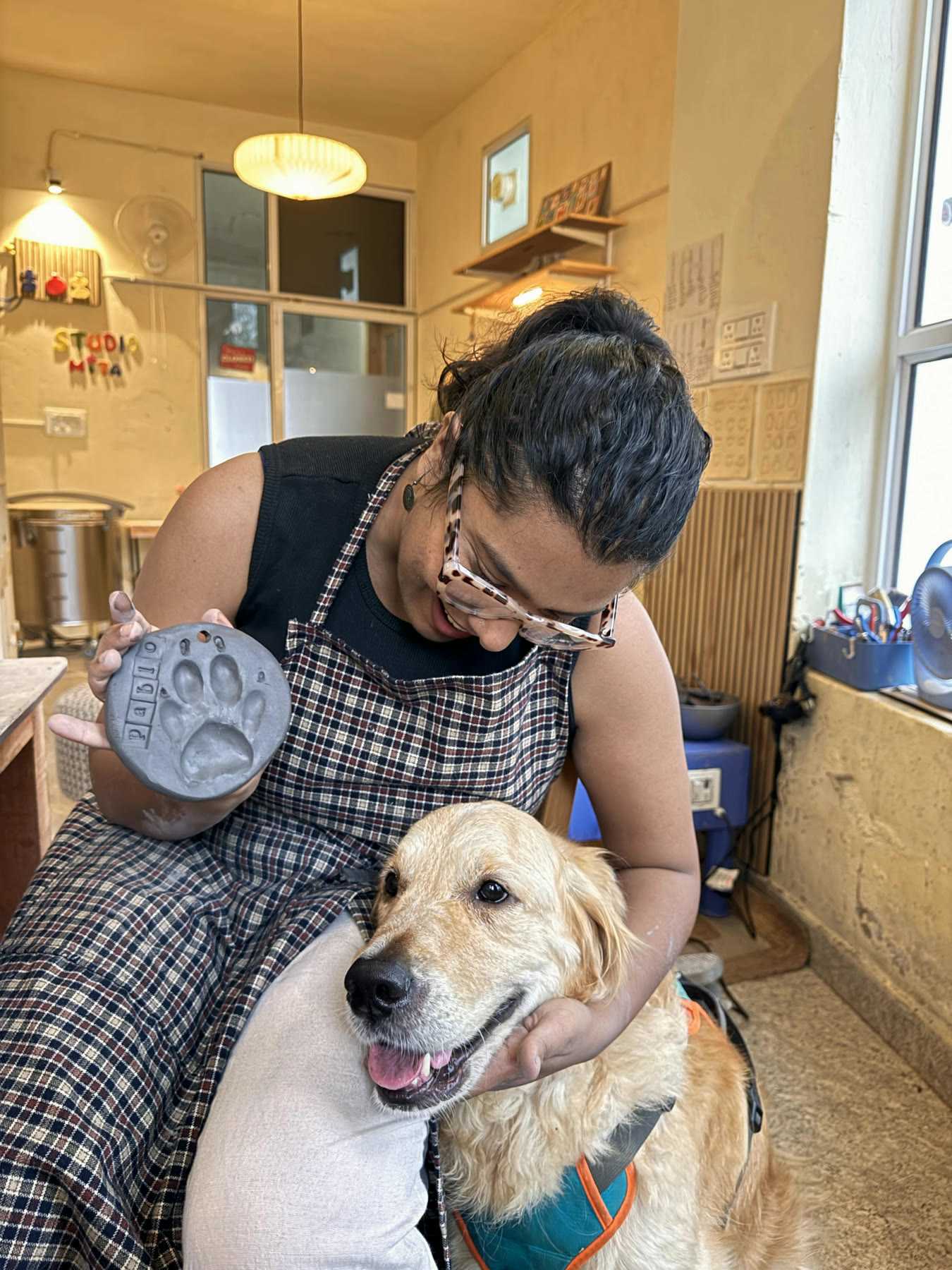 A guest with her arms around the studio's golden retriever, a paw-print clay piece in her hand