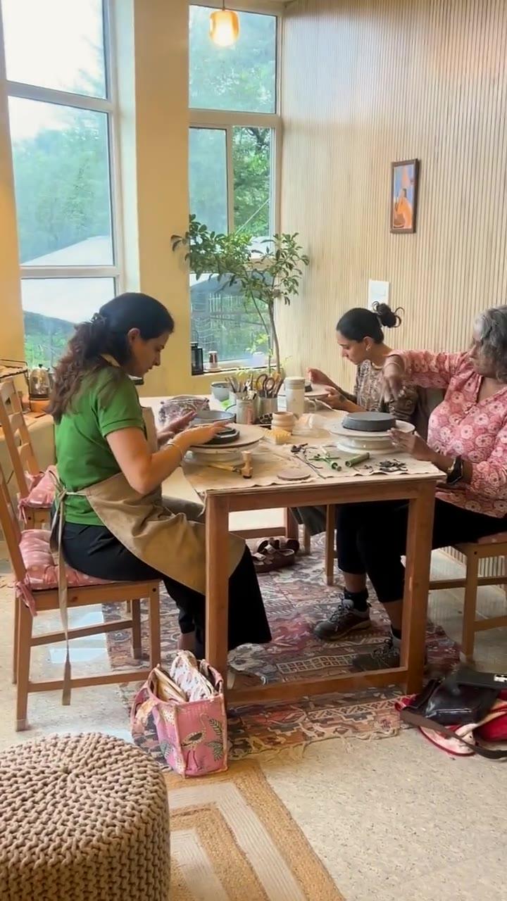 Three people working clay together at the long studio table, the valley through the windows behind them