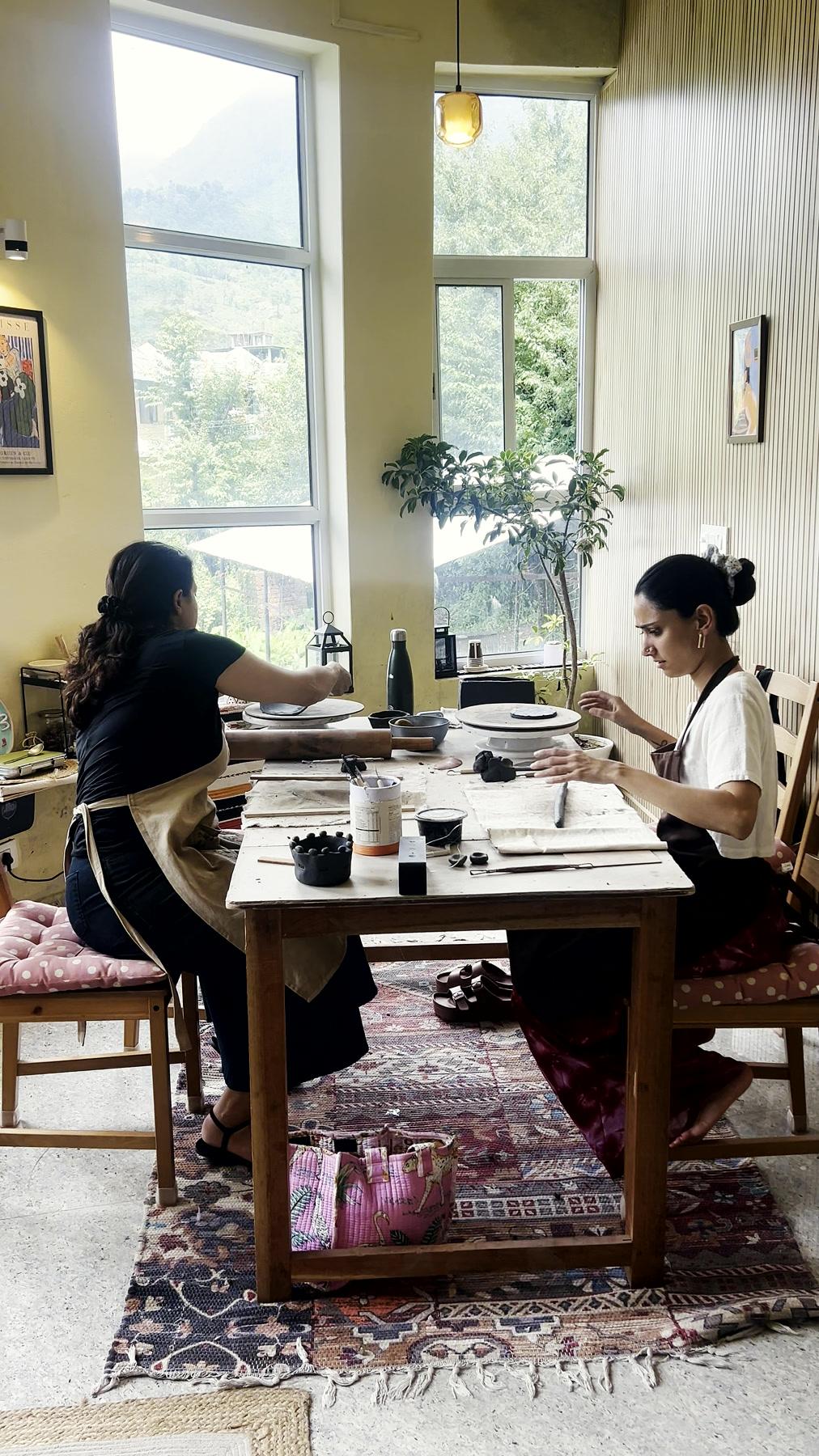 Two students working at the studio's long table, the Dhauladhars visible through the windows