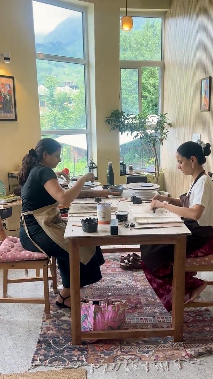 Madhumita crossing the studio behind a guest working alone at the wheel