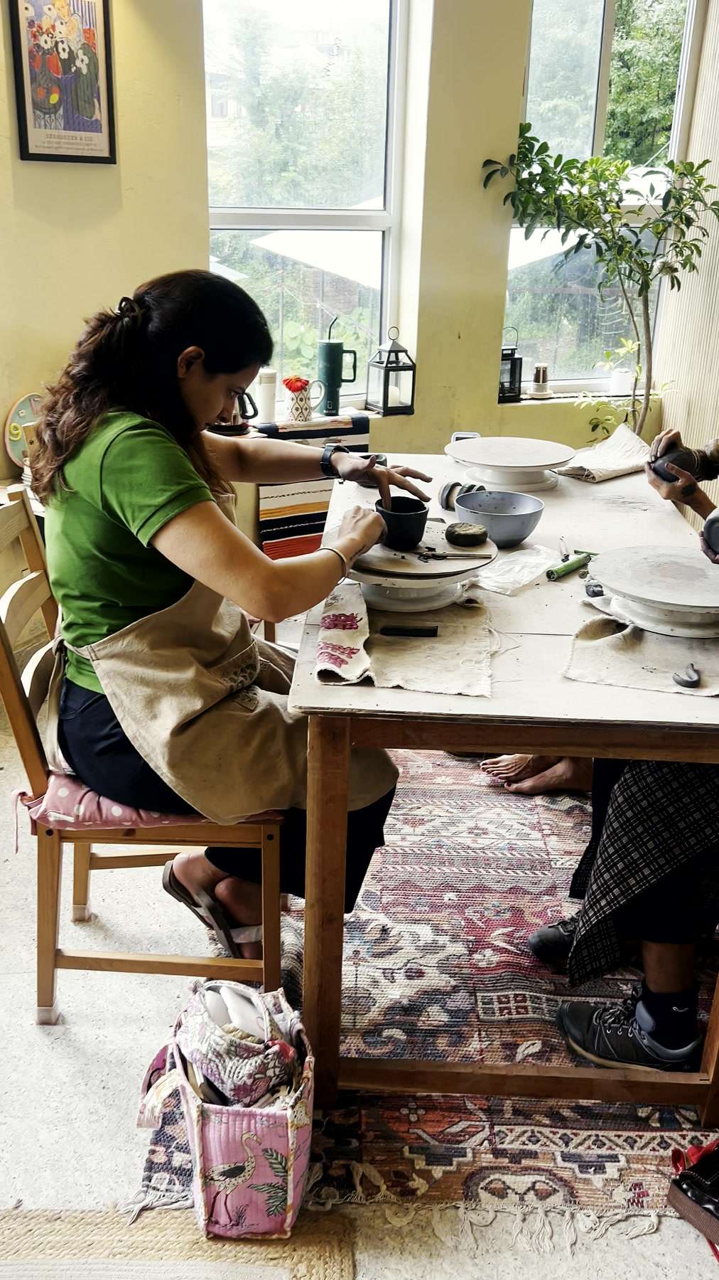Two people working clay across the studio table, mountain light through the windows