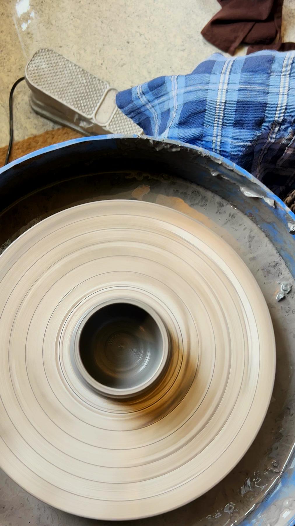 Looking down at two hands steadying a cylinder rising on the wheel